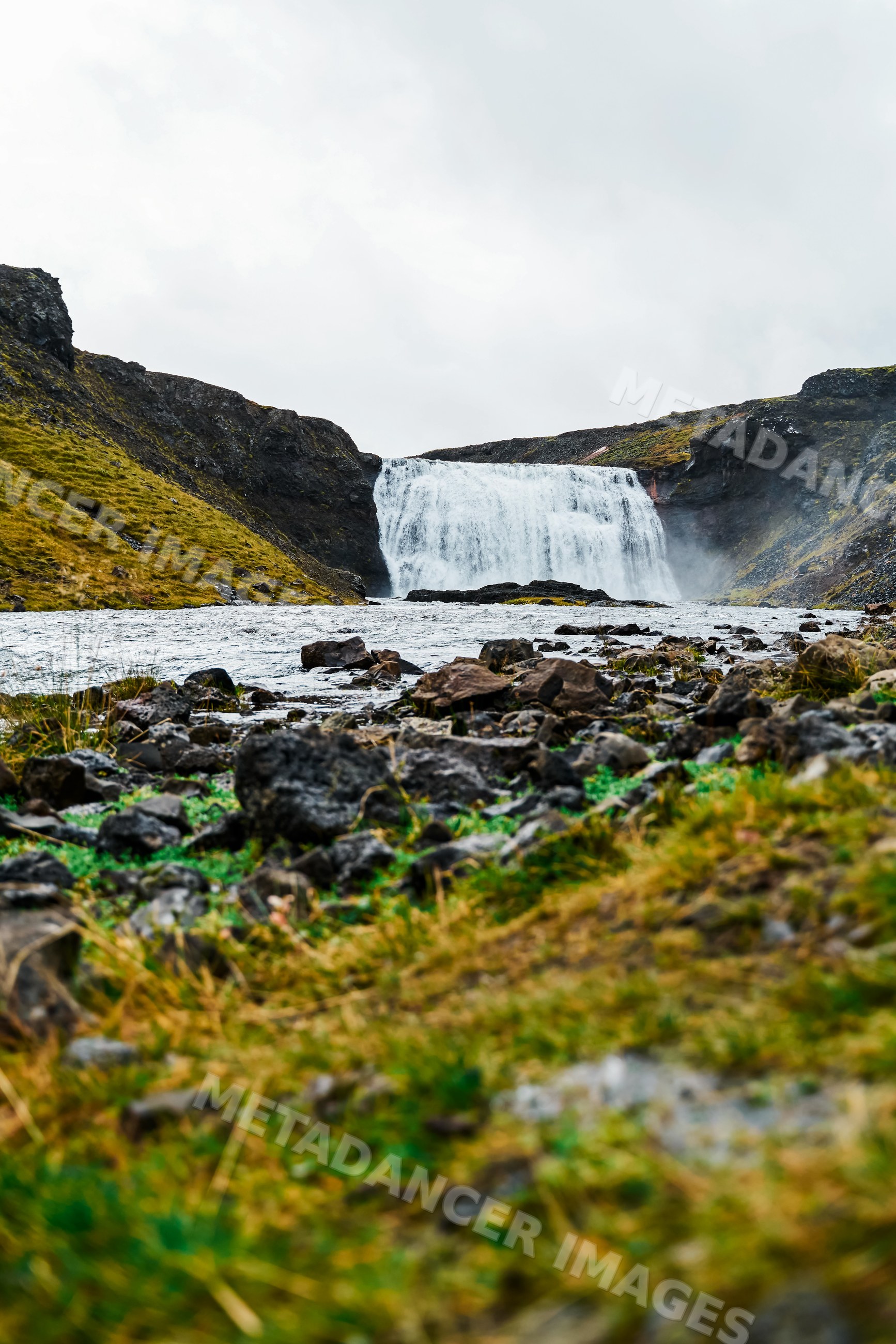 Waterfall flowing into a rocky river with green grass
