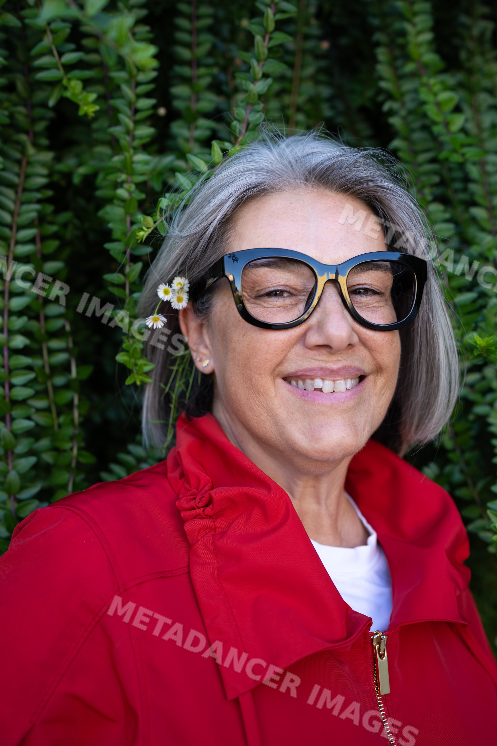 Smiling white woman in red jacket with flower in hair outdoors
