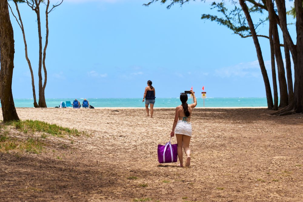 White woman walking on tropical beach with purple bag
