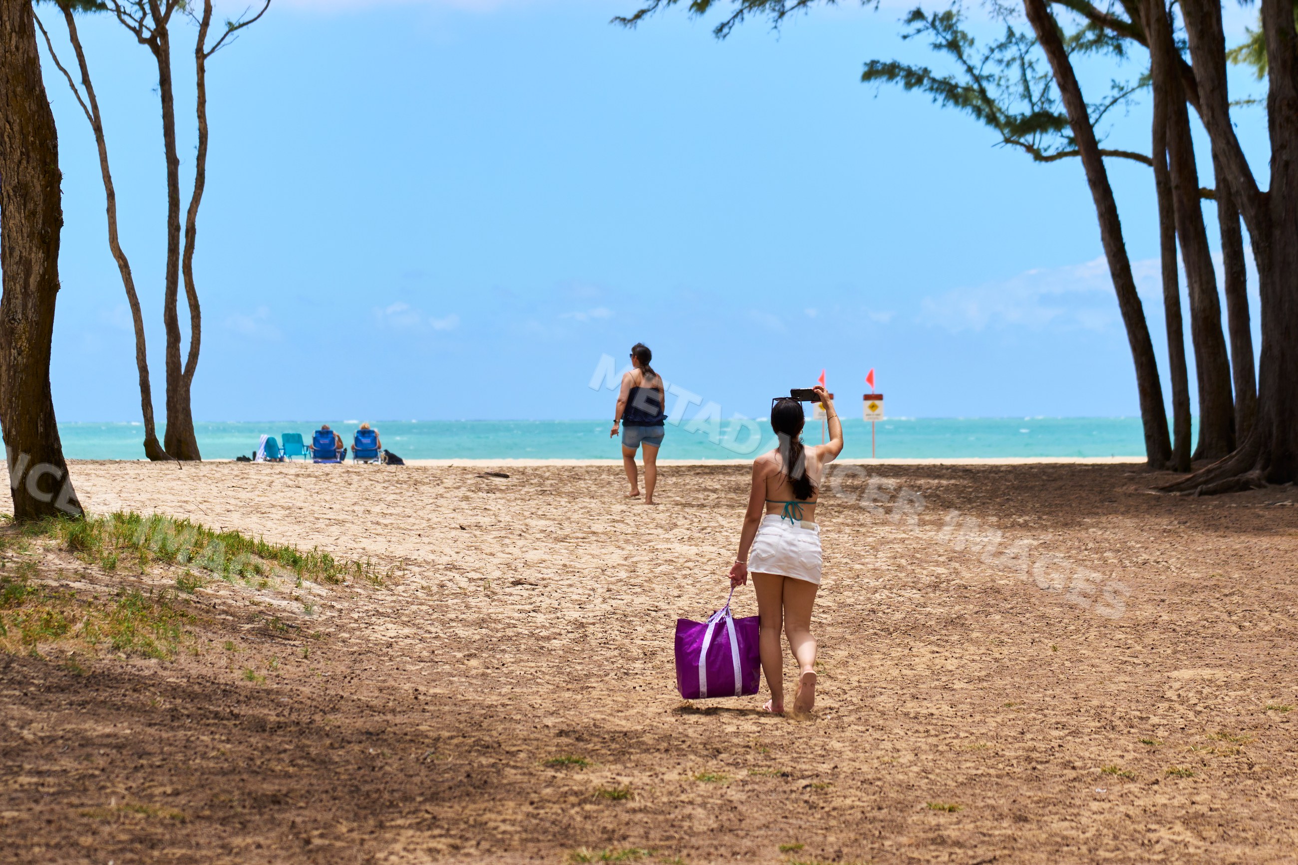 White woman walking on tropical beach with purple bag