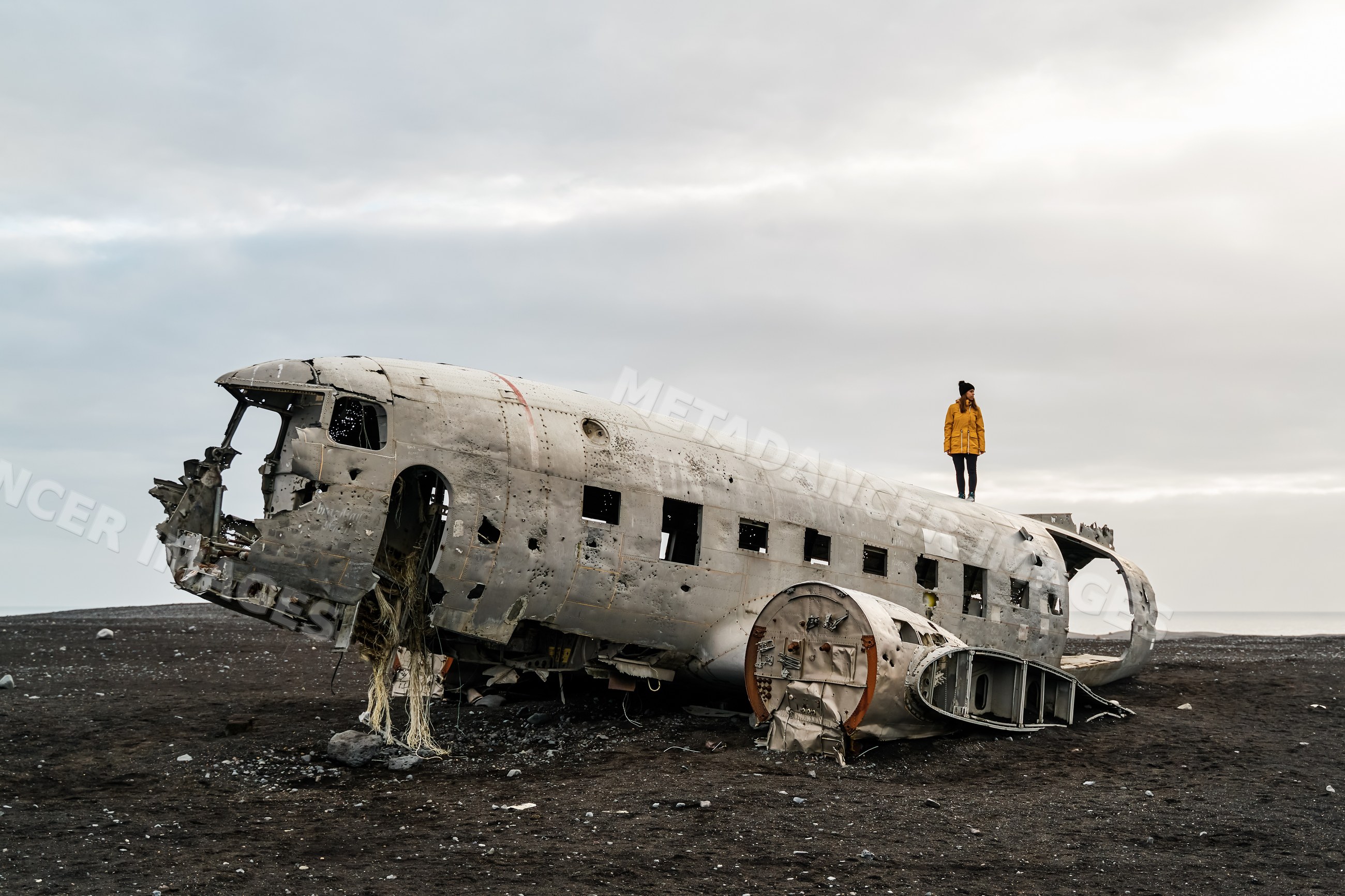 White Woman standing on abandoned airplane wreckage on black sand