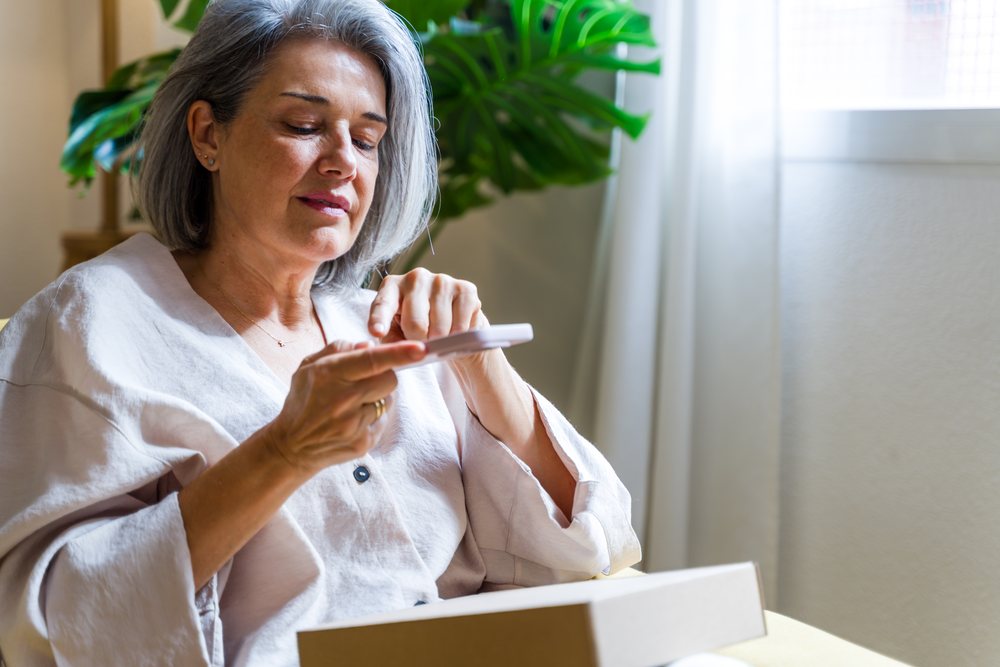 White woman reading a card near window with indoor plant