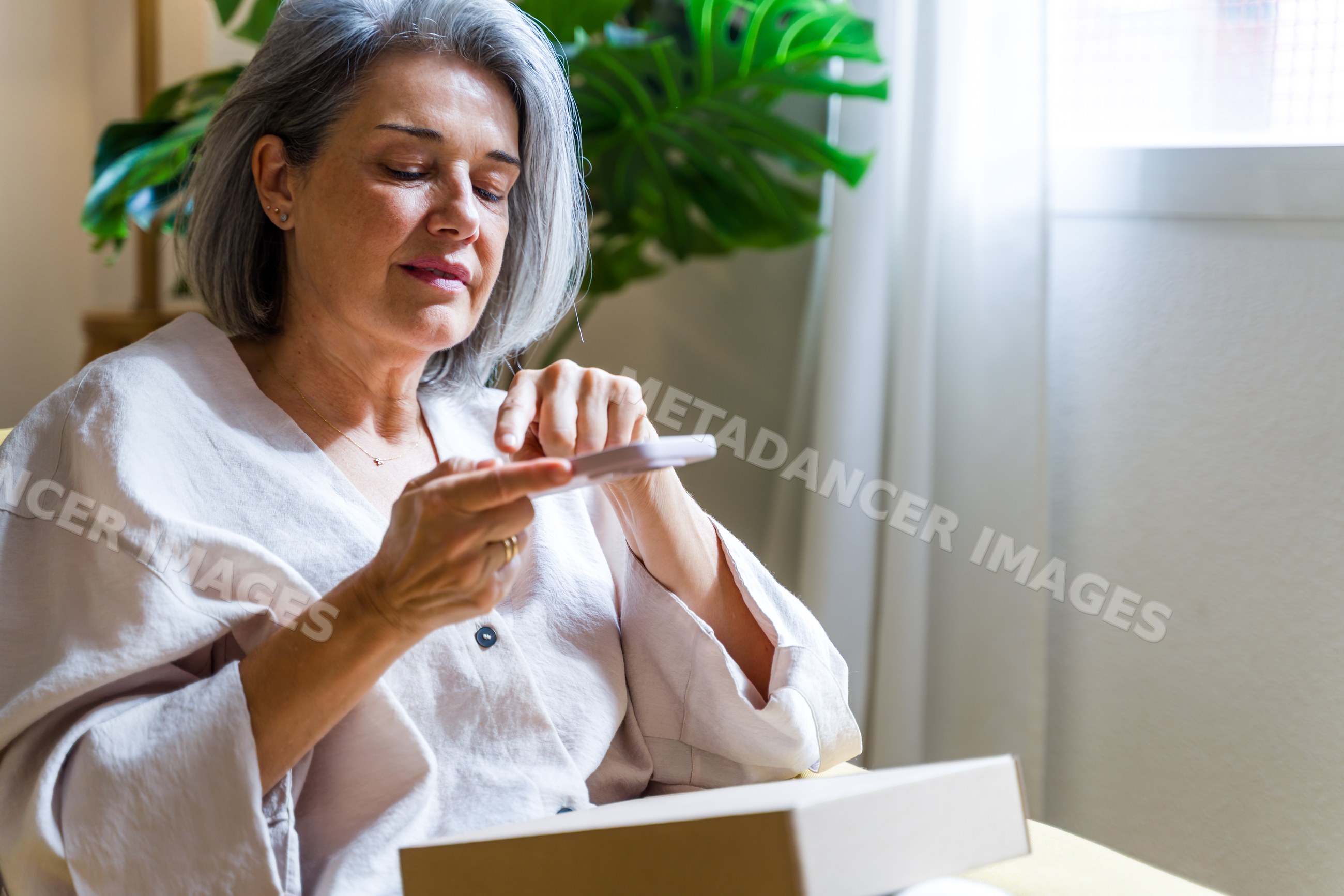 White woman reading a card near window with indoor plant