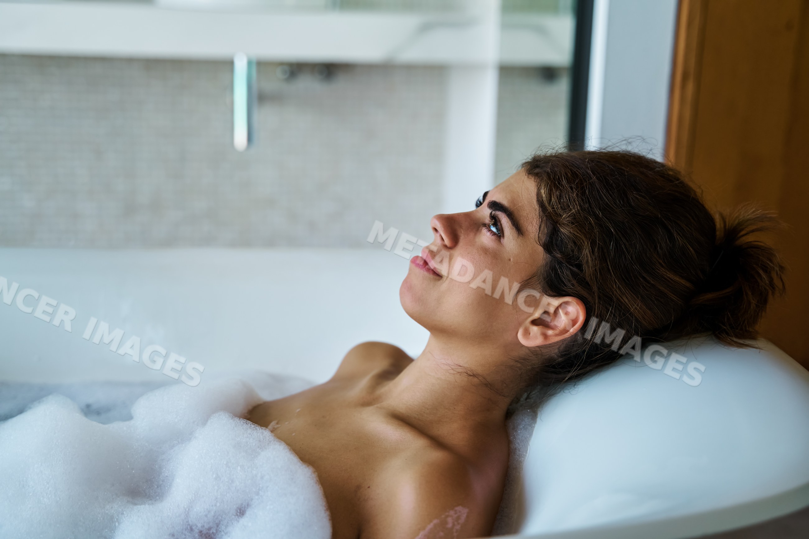 A young white woman relaxes in a bubble bath in a modern bathroom spa
