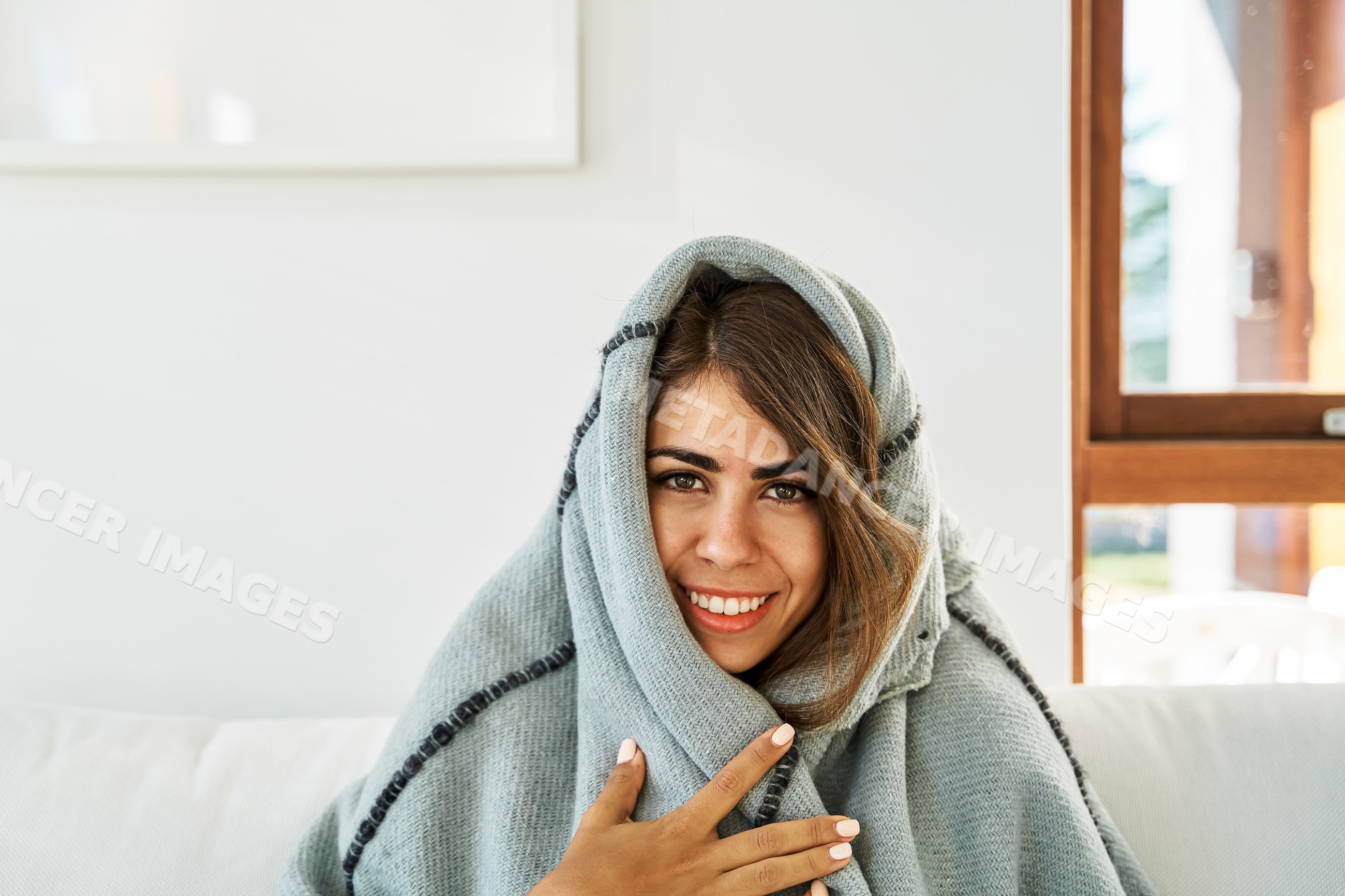 A white woman wrapped in a blanket smiles warmly indoors