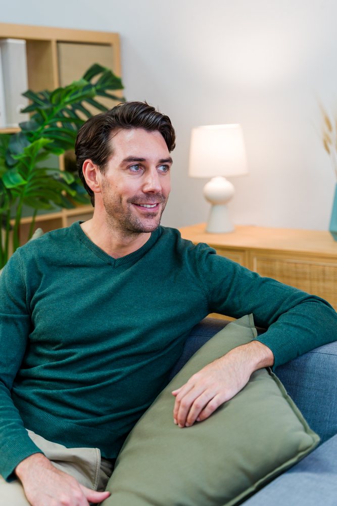 White man sitting on couch smiling in living room interior