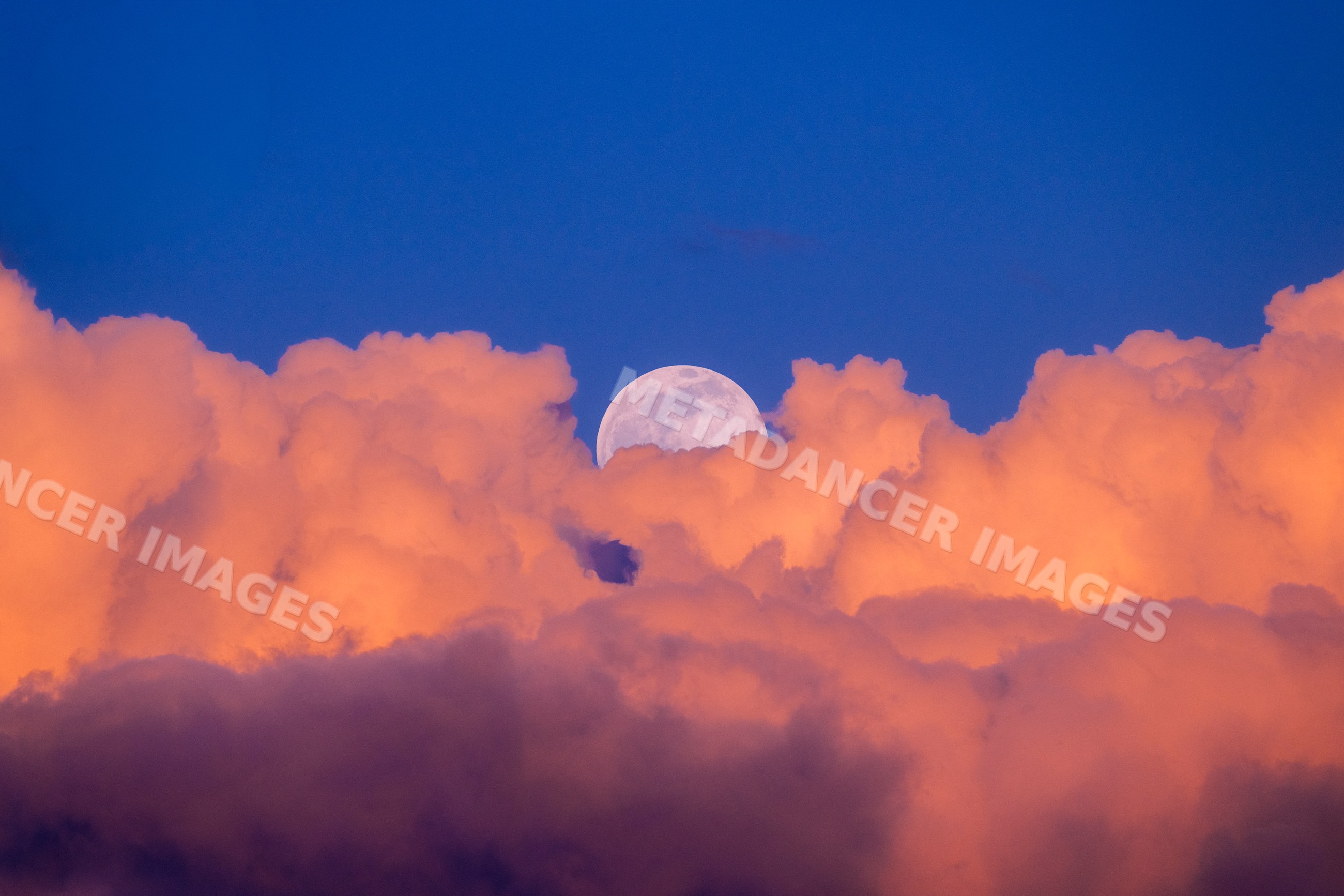 Moon rising above illuminated clouds in evening sky over Seattle, USA
