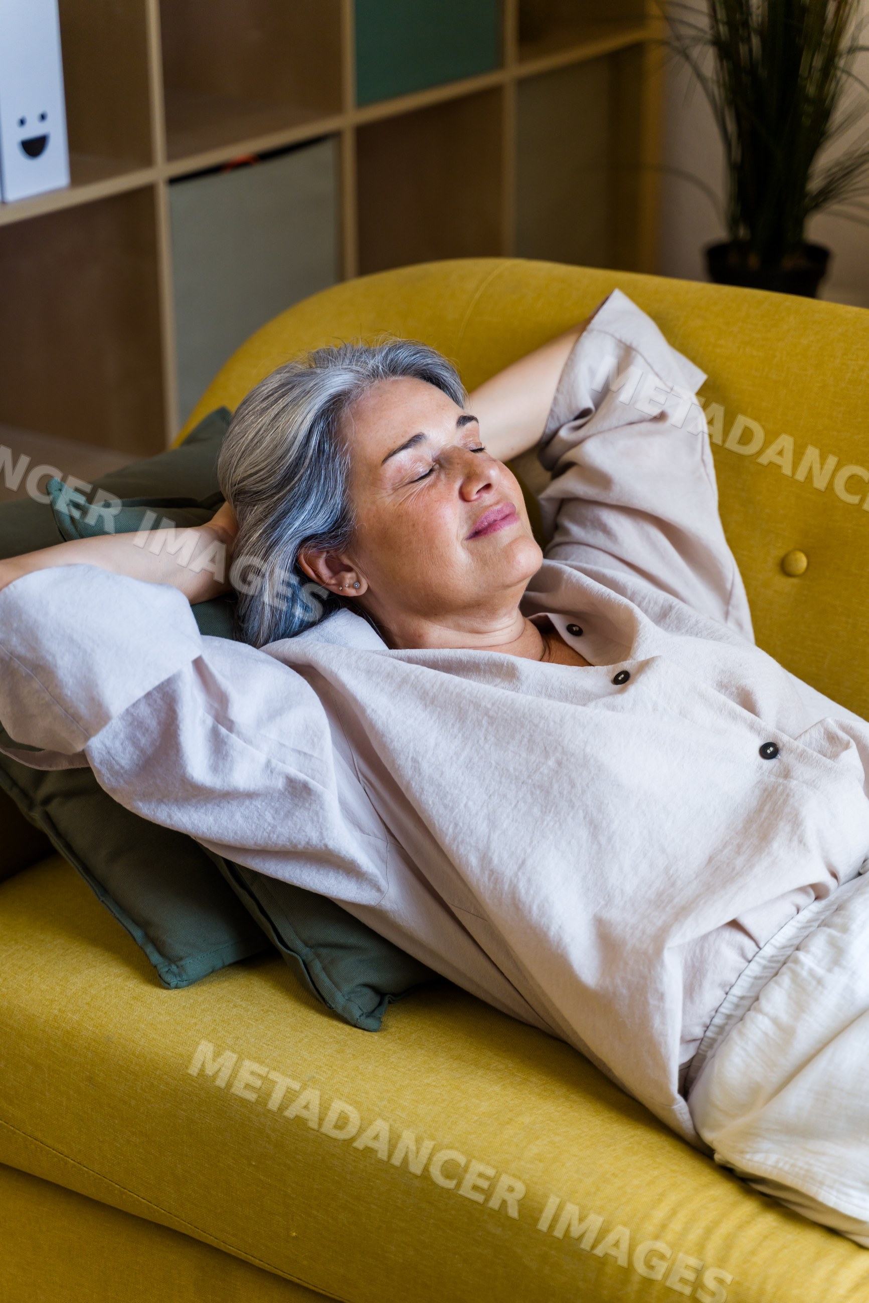 White woman relaxing peacefully on yellow sofa indoors