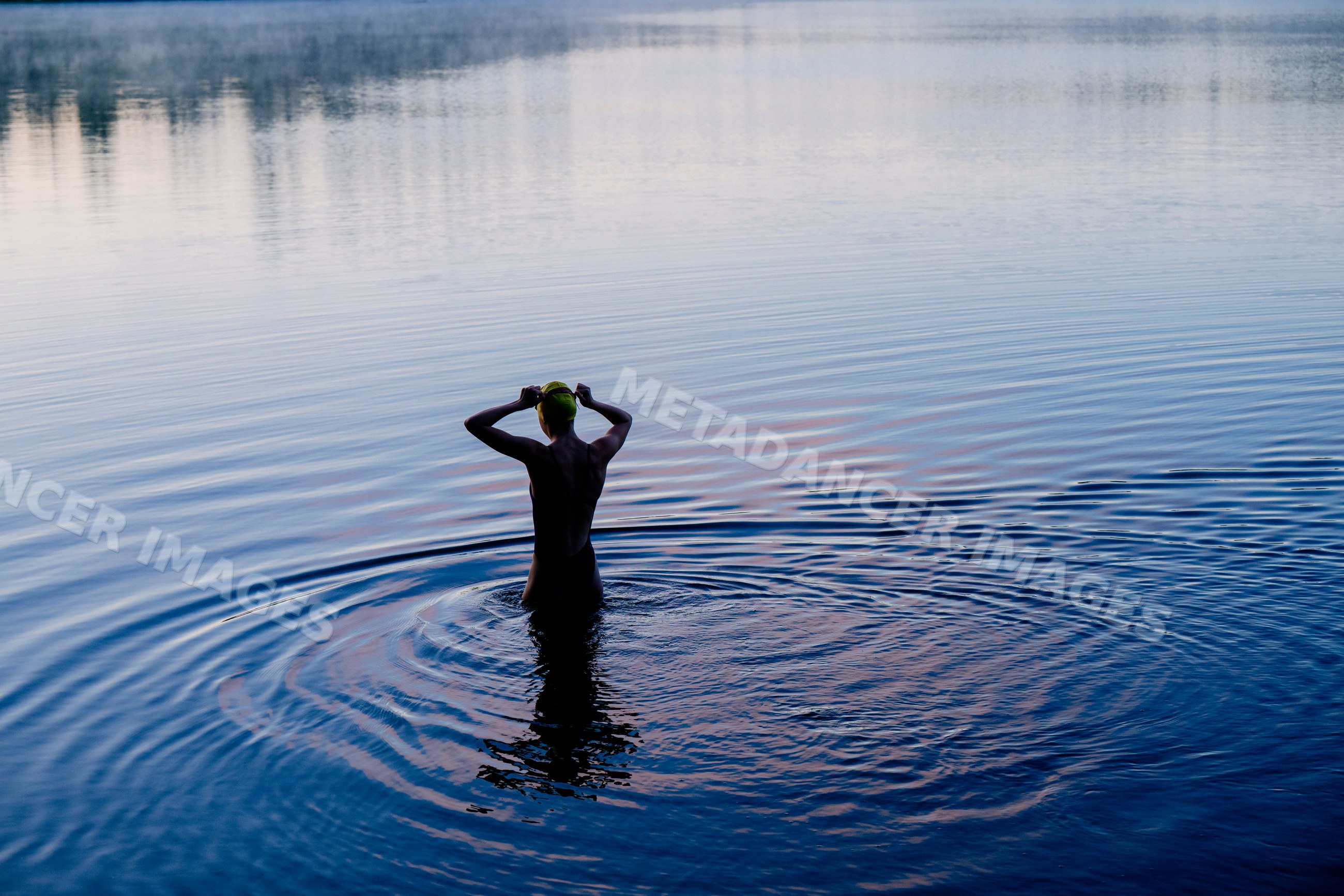White woman standing in lake putting on swim cap with rippling water
