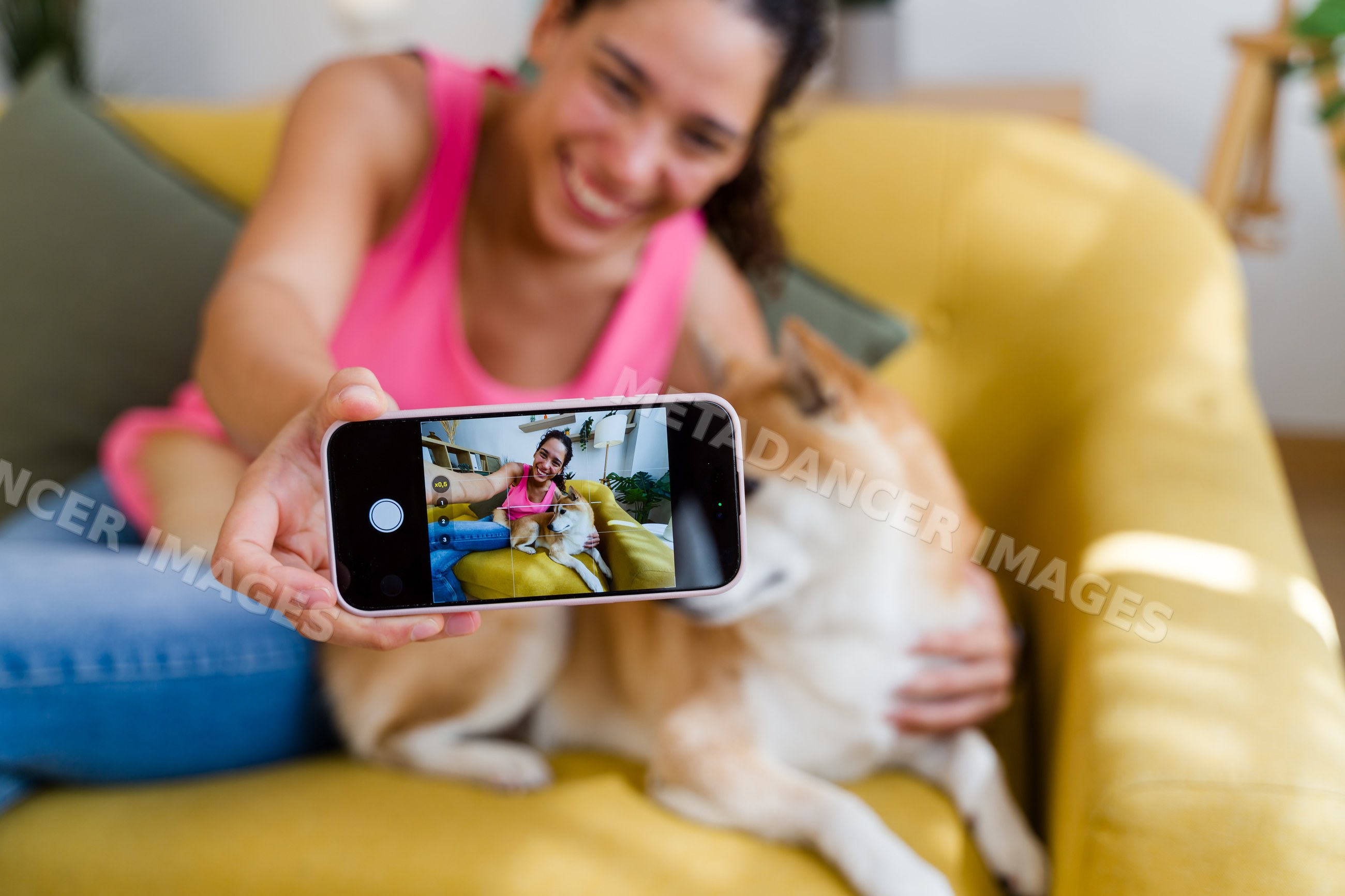 A Hispanic woman takes a selfie with her dog on a yellow couch