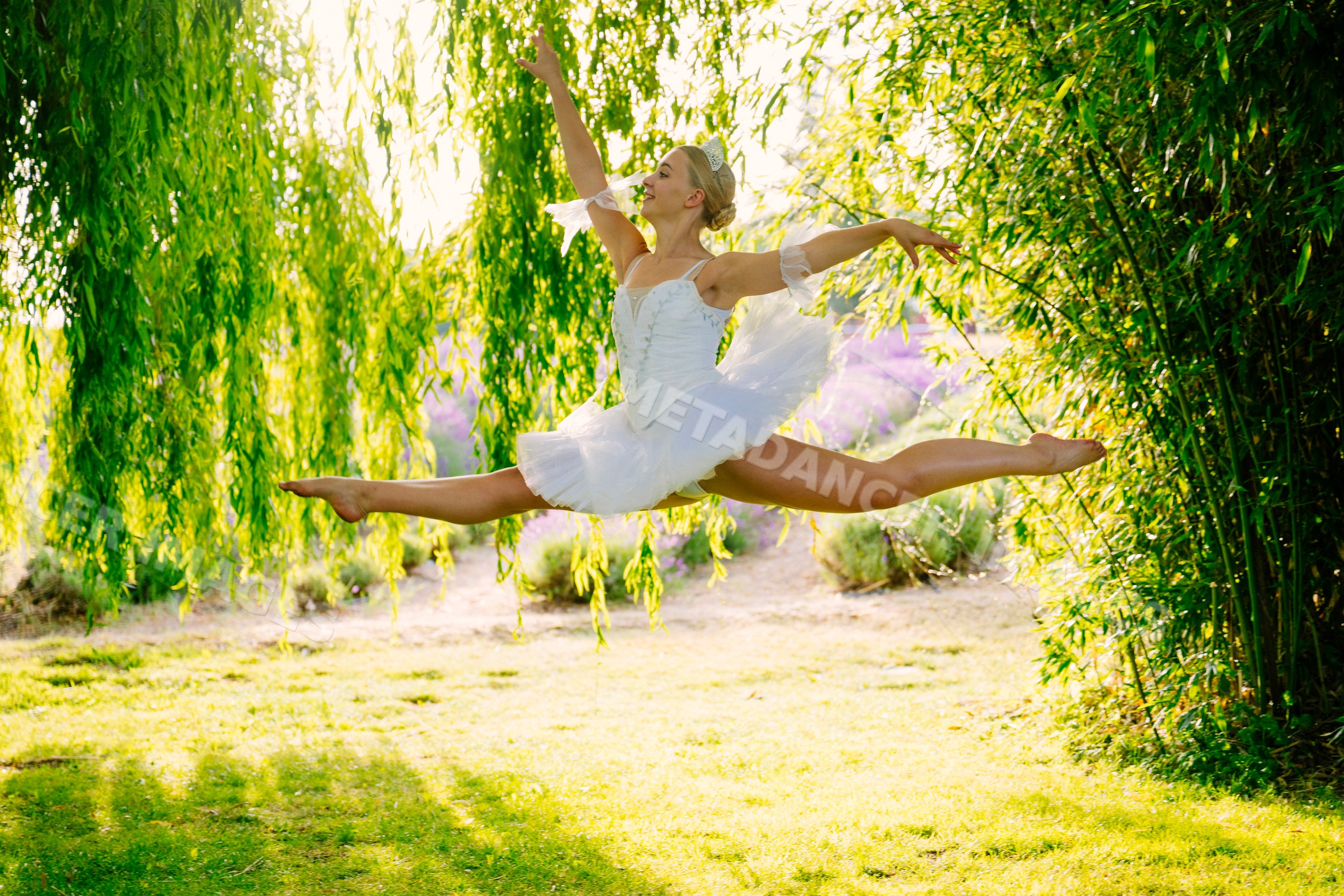 A ballerina leaps gracefully outdoors under a willow tree in WA, USA