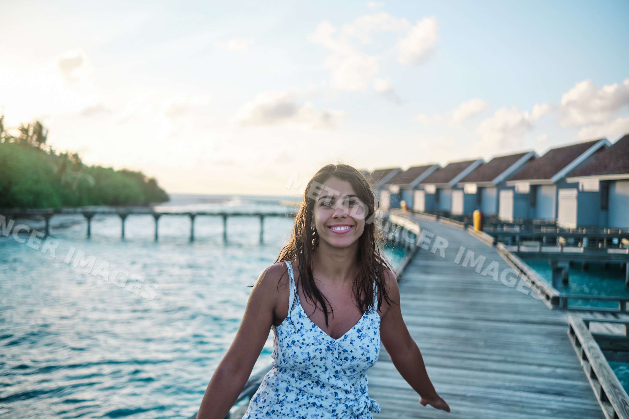 A white woman walking on a wooden pier near overwater bungalows