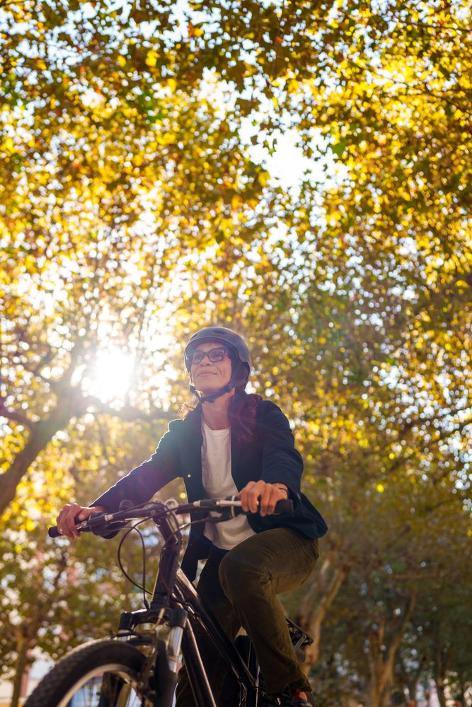 Hispanic woman riding bicycle in sunlit Málaga park with autumn leaves