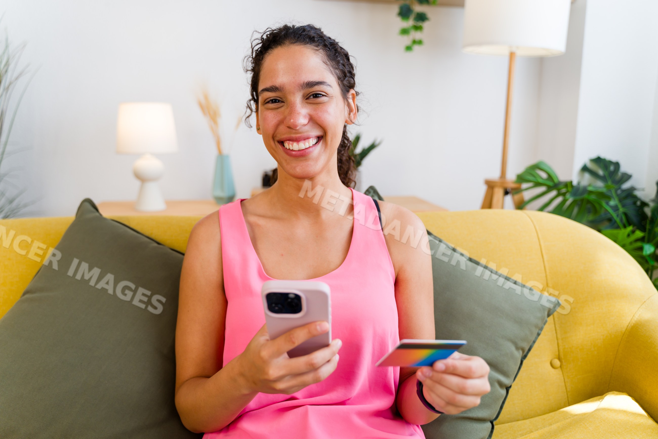 A smiling Hispanic woman uses a mobile phone and credit card