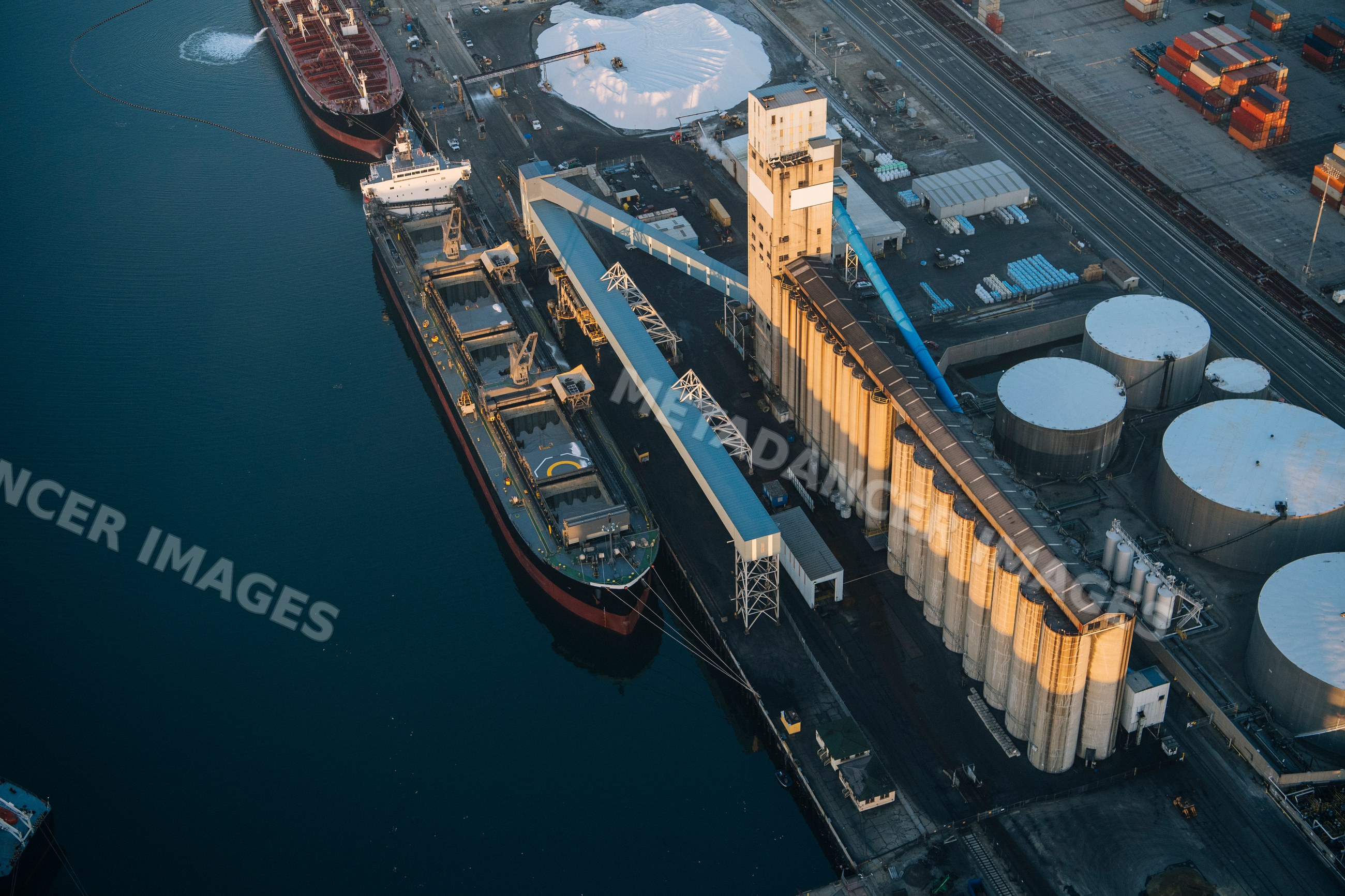 A cargo ship docked at an industrial port next to grain silos in Long