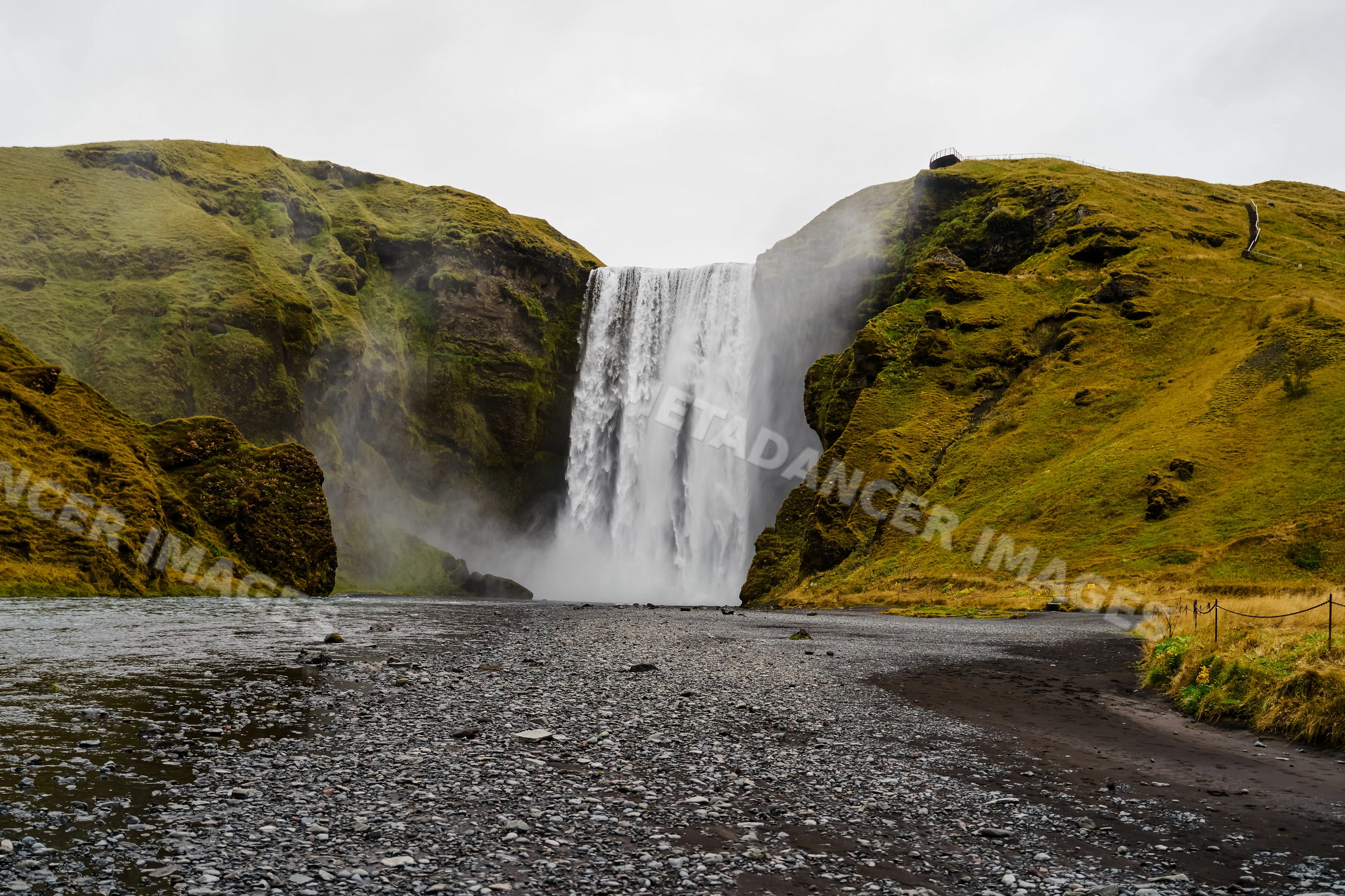 A powerful waterfall flows down mossy cliffs into a rocky riverbed