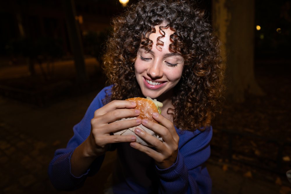 White woman smiling while eating a burger outdoors at night in Madrid