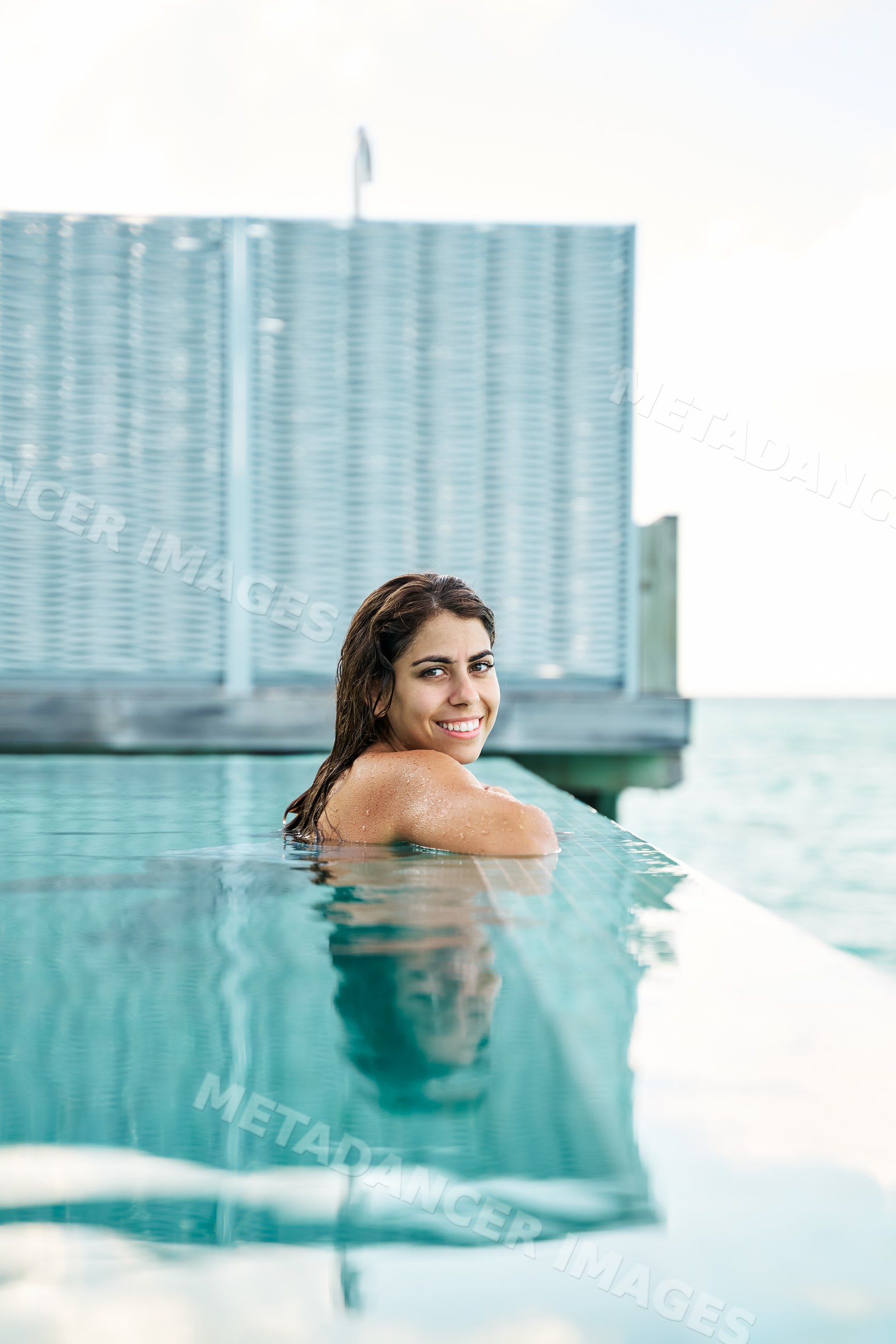 A white woman relaxes and smiles in an infinity pool with ocean views