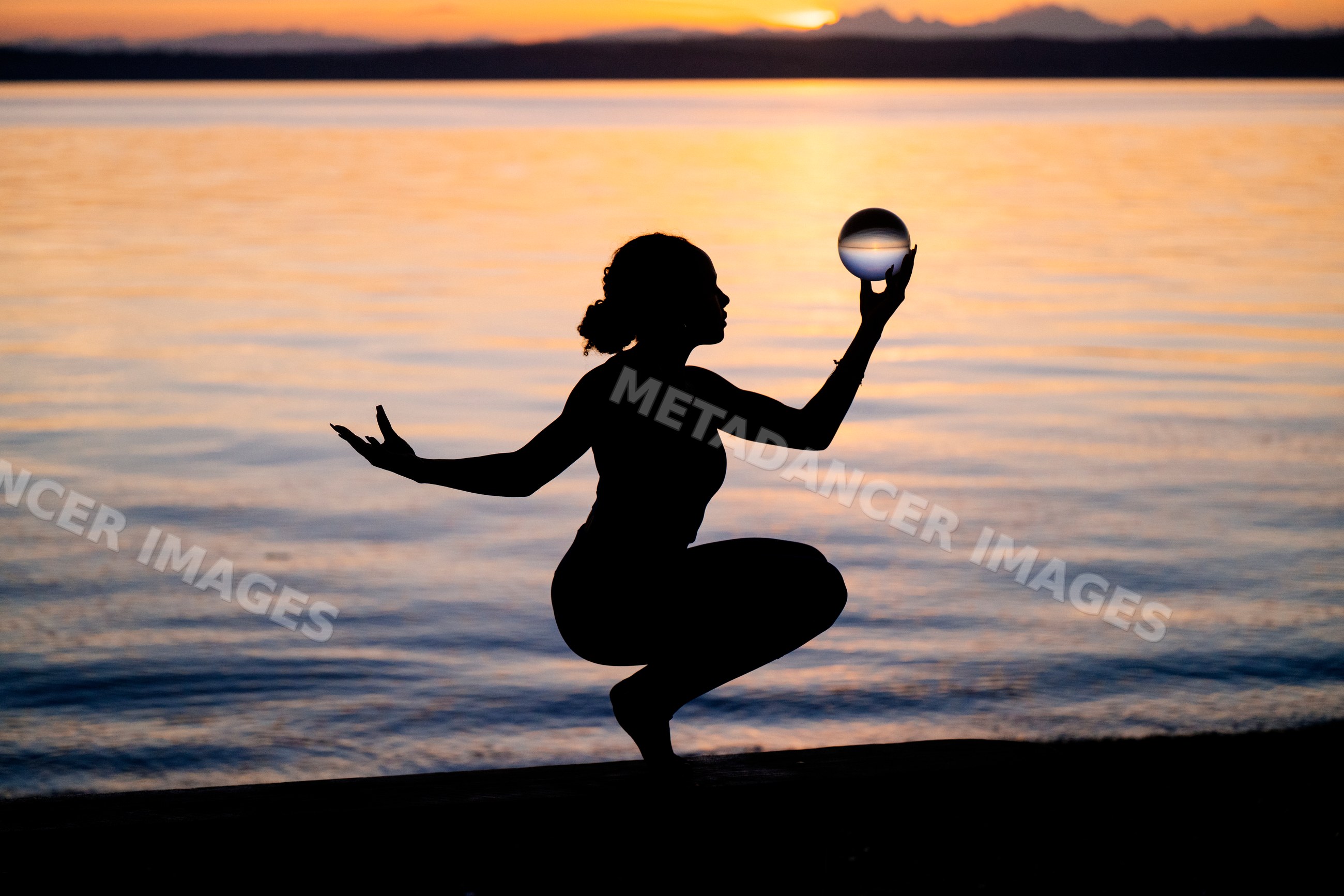 Silhouette of Hispanic woman balancing yoga pose with glass sphere