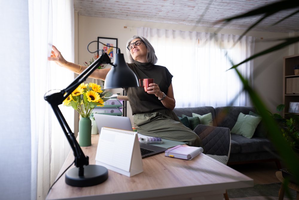 White woman drinking coffee sitting by the window in home office