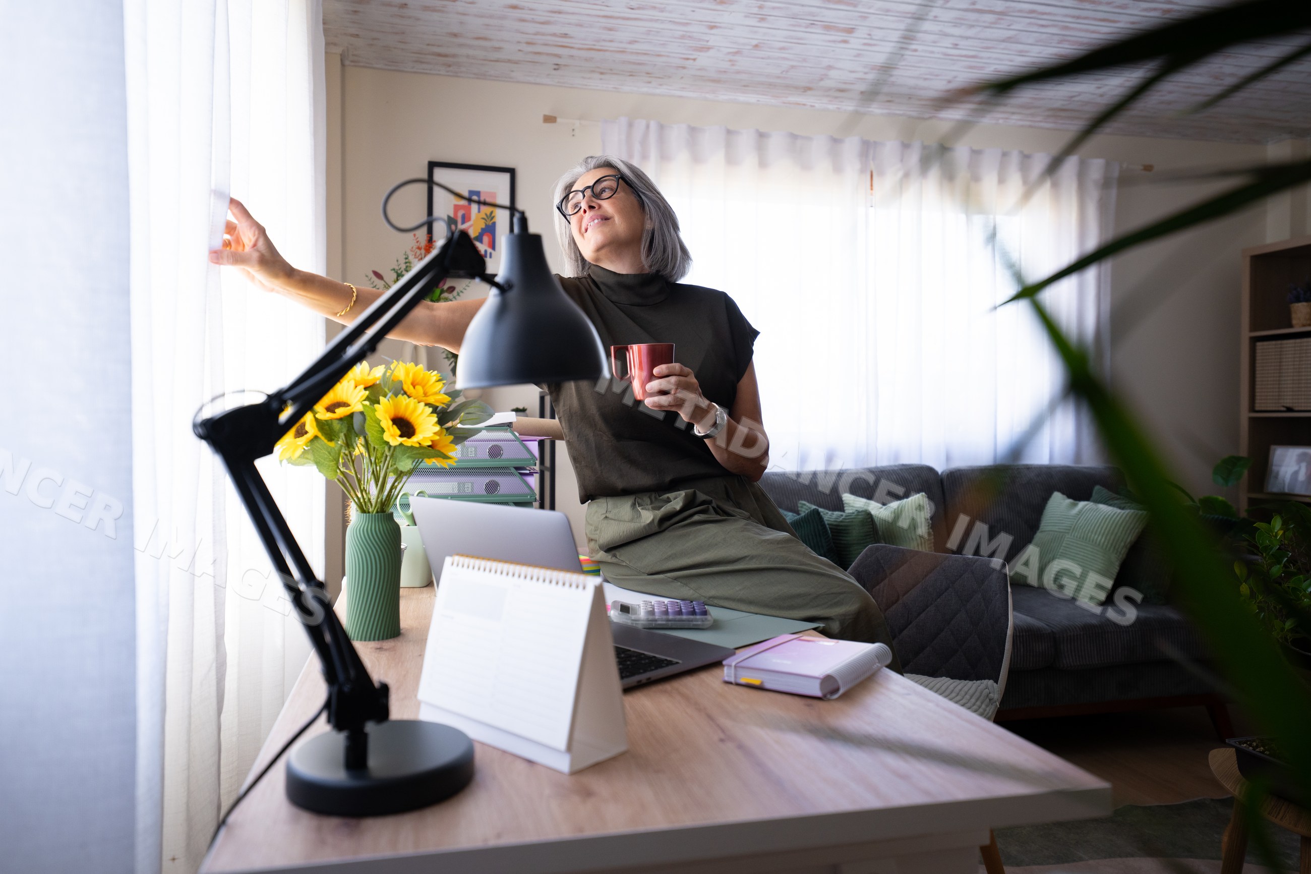 White woman drinking coffee sitting by the window in home office