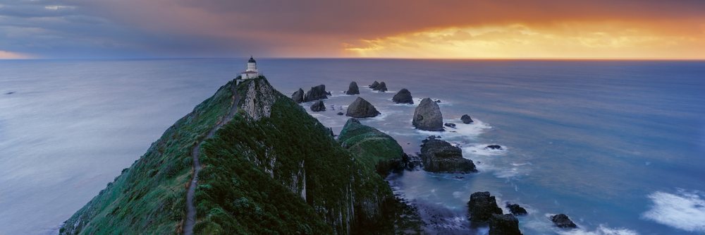 Lighthouse on hill overlooking ocean rocks