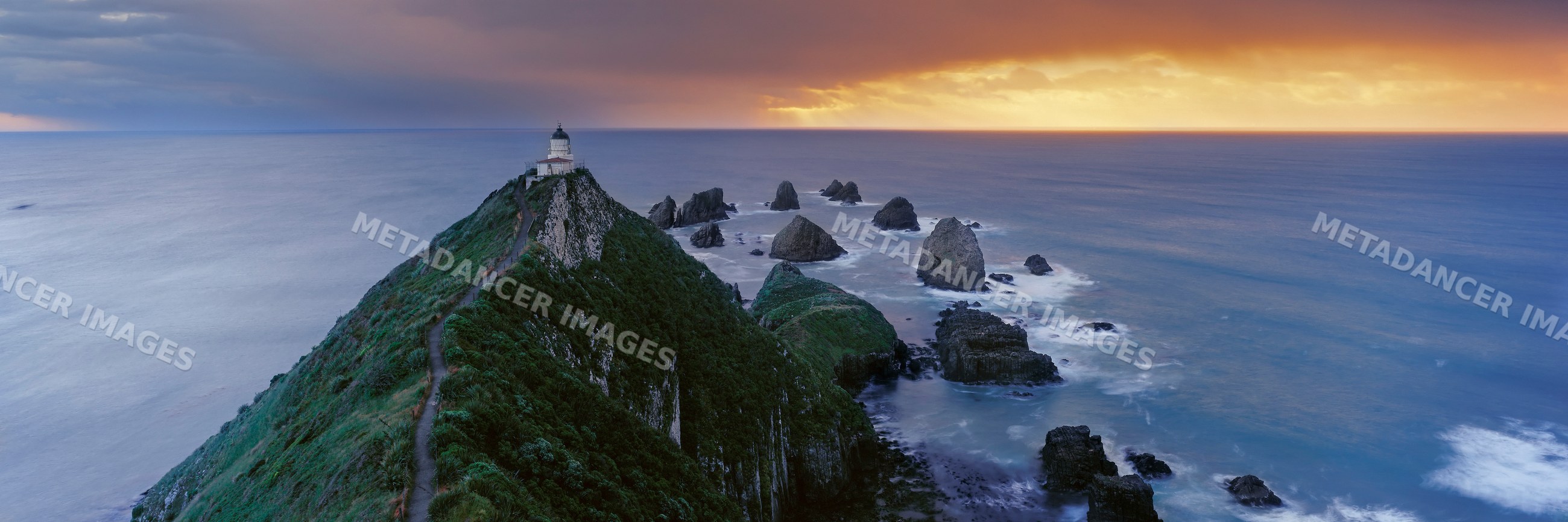 Lighthouse on hill overlooking ocean rocks