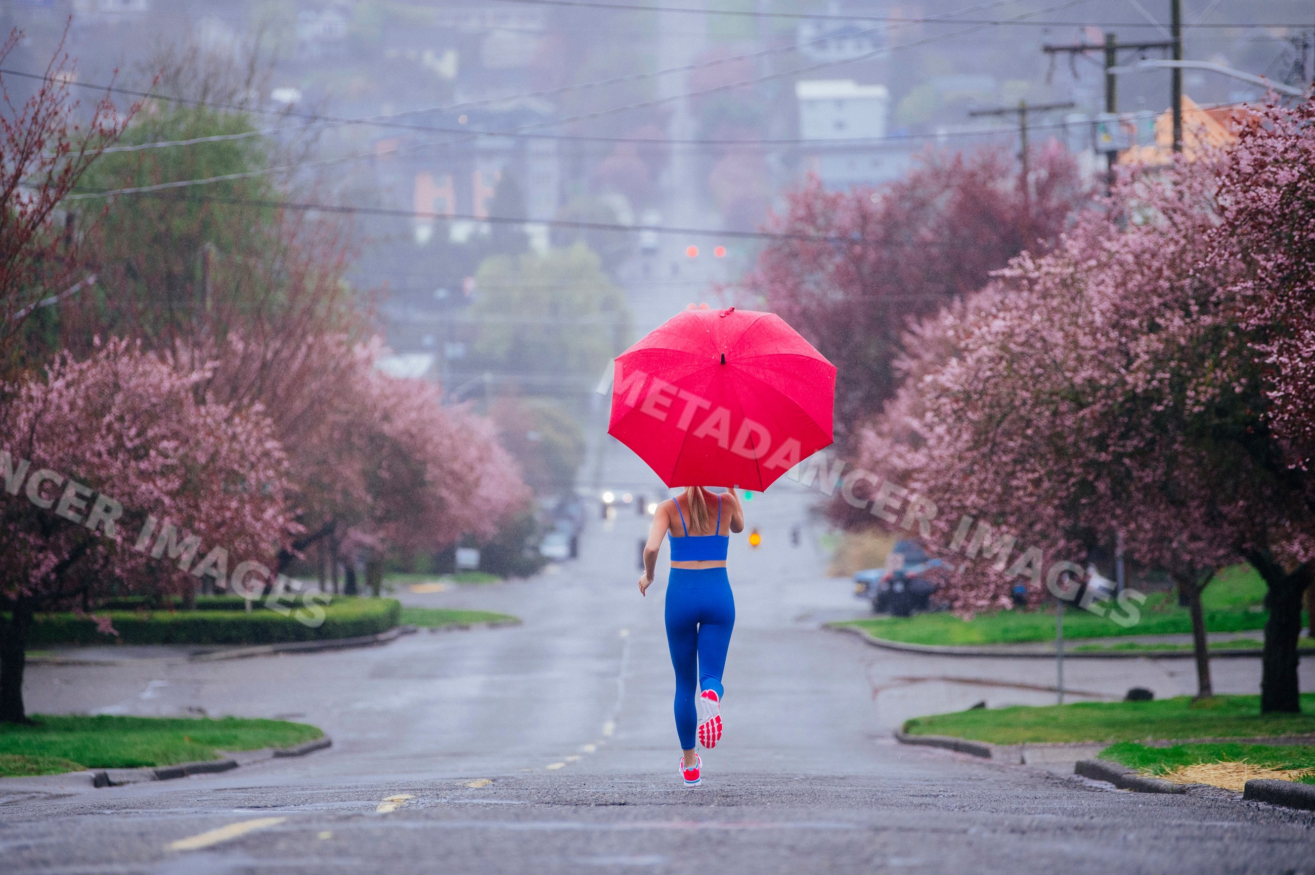 White woman running with red umbrella on rainy street with blooming