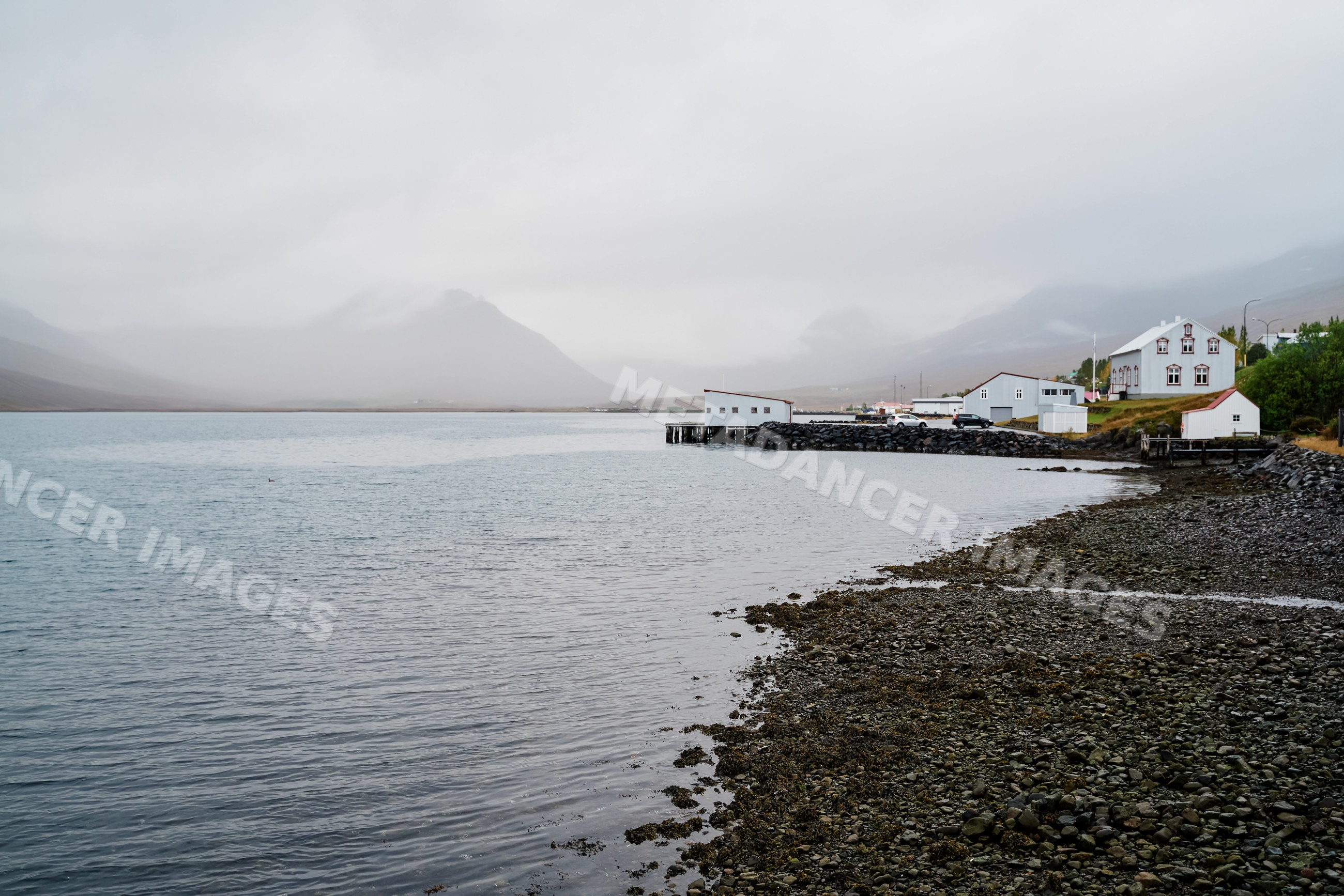 Calm coastal village with houses and pier on foggy rocky shore