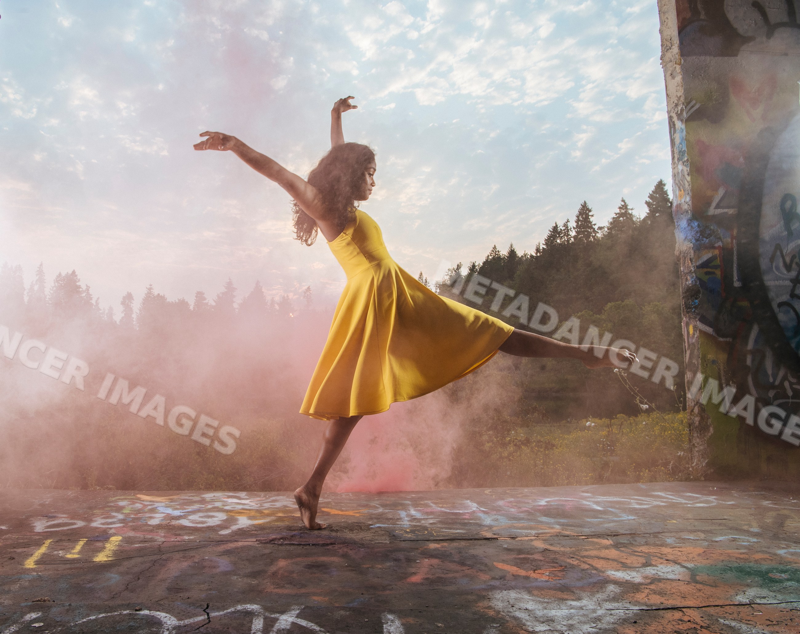 South Asian dancer in yellow dress performing outdoors near graffiti