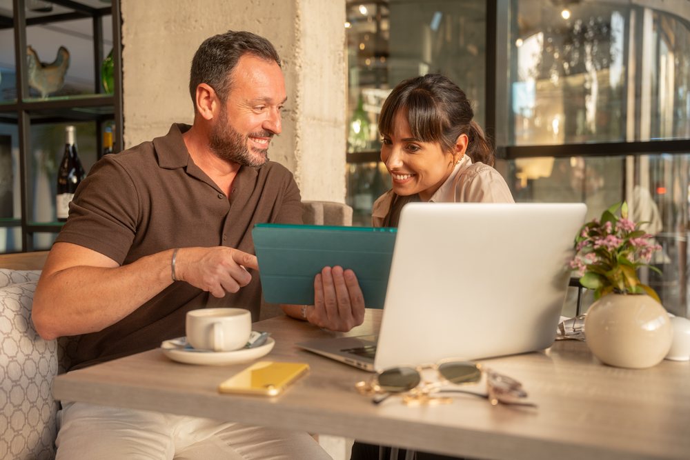 Coworkers sharing tablet at cafe table with coffee and laptop