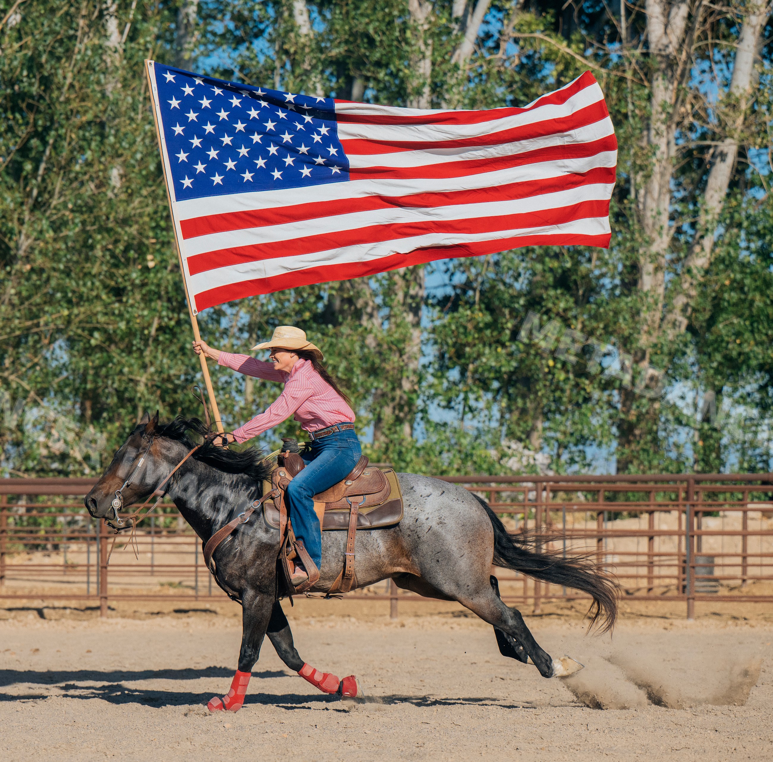 White woman riding horse holding american flag in rodeo arena outdoors