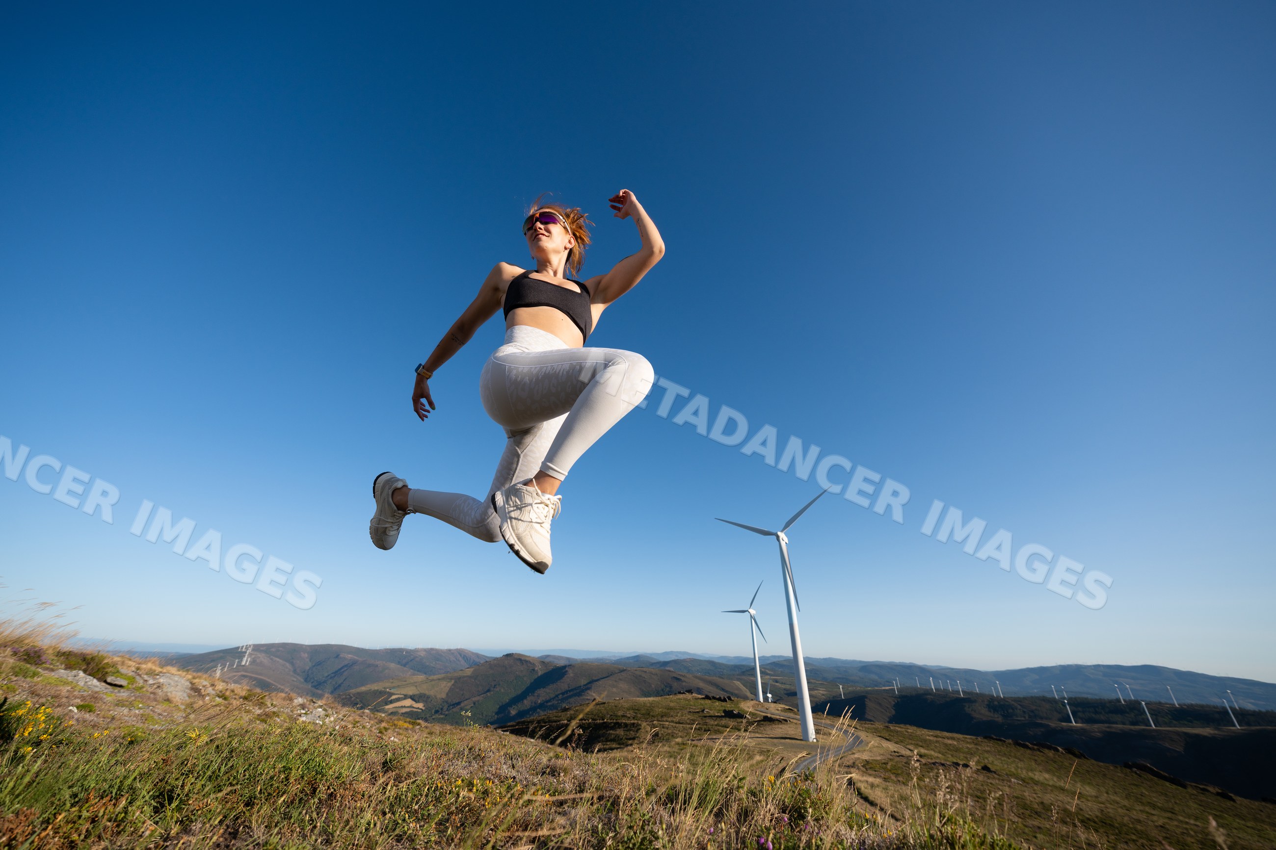 White Woman jumping actively outdoors near wind turbines in Galicia