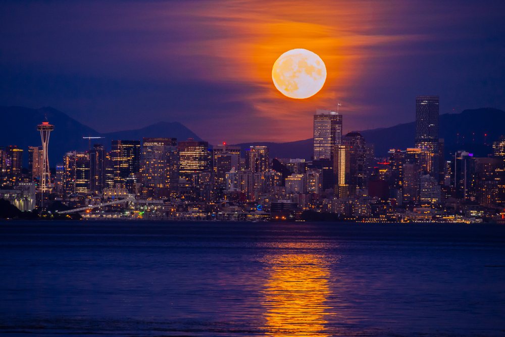 Full moon rising over Seattle skyline with water reflection