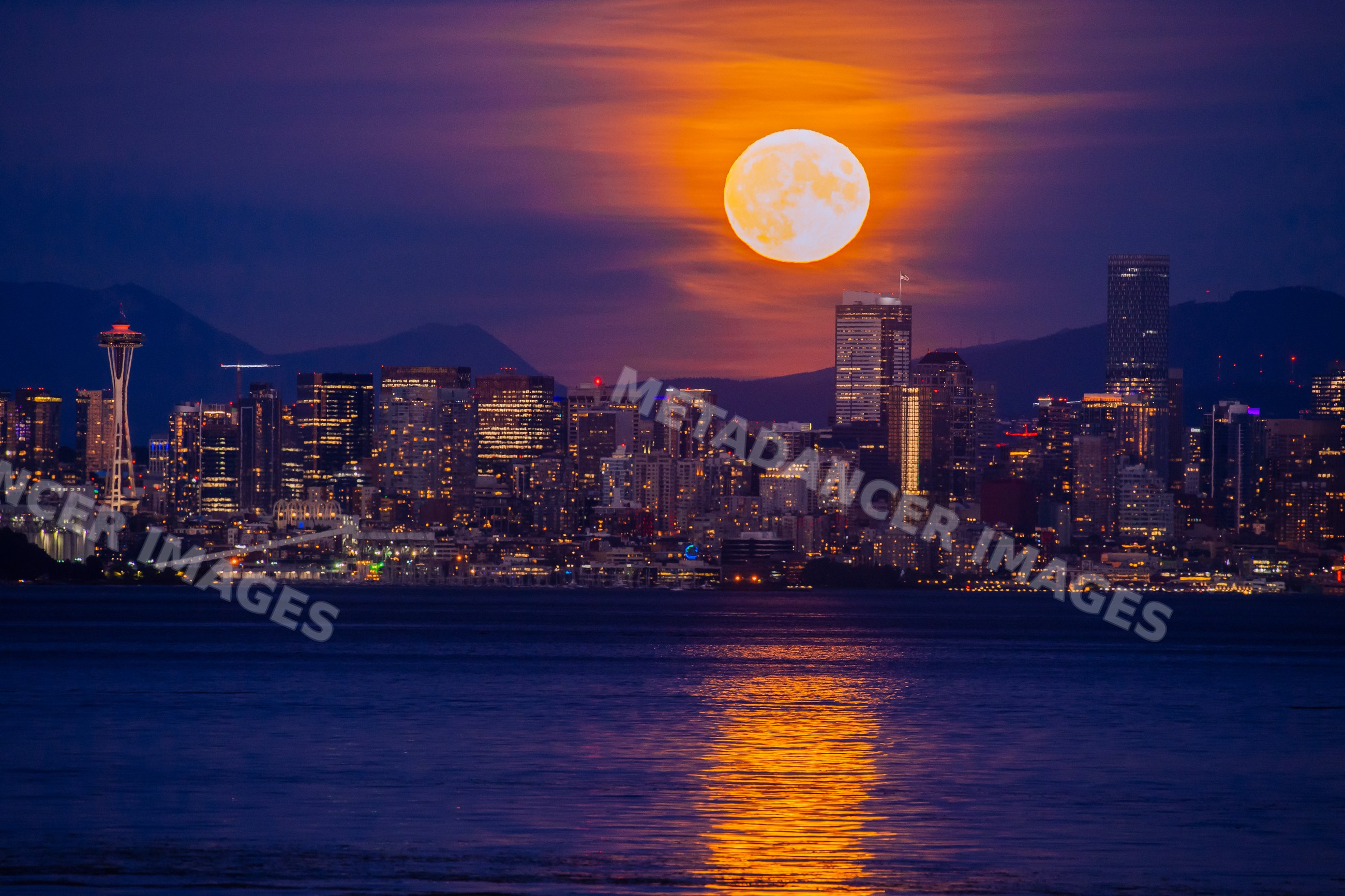 Full moon rising over Seattle skyline with water reflection