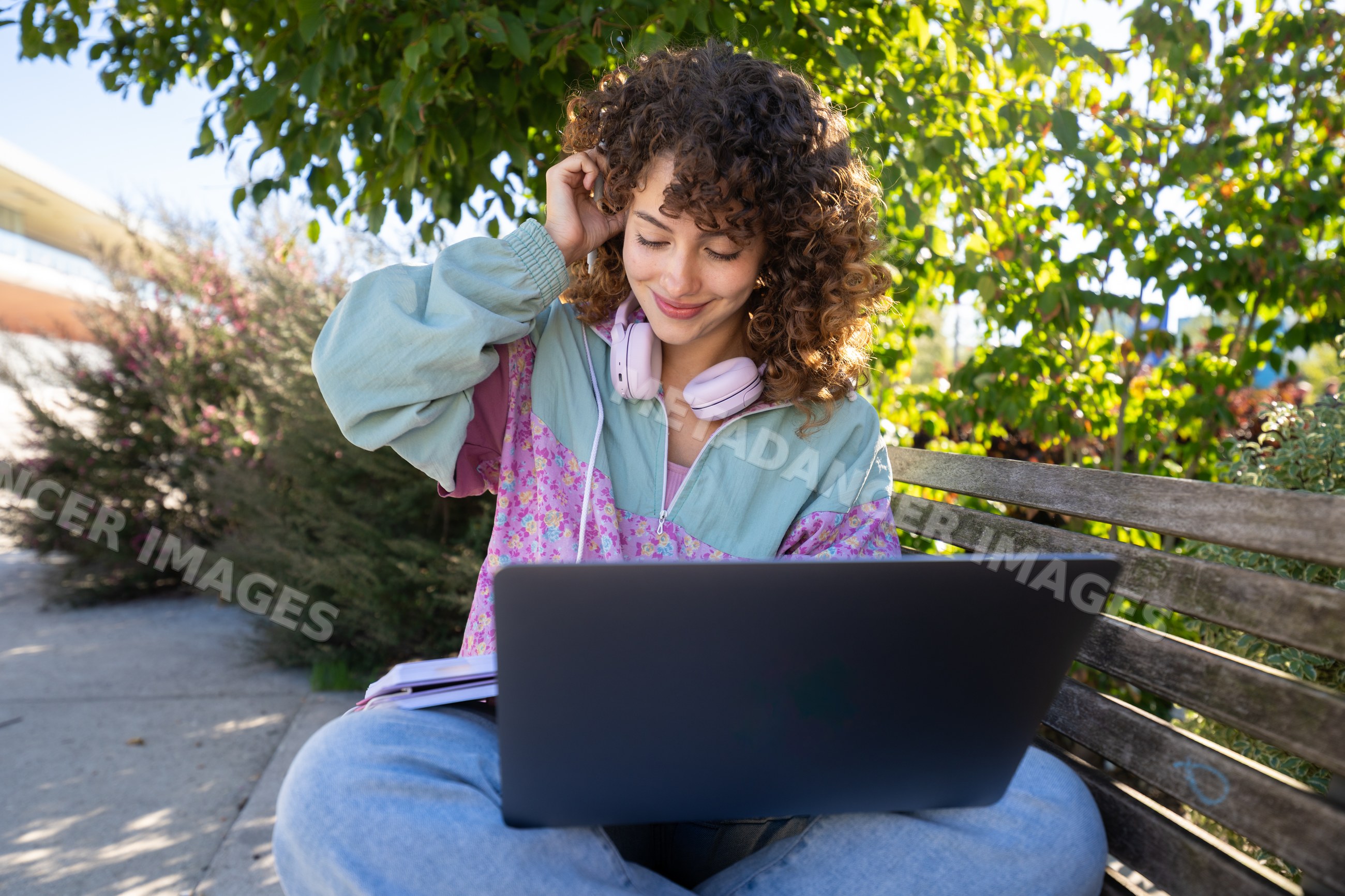 White woman sitting on a bench outdoors using laptop with headphones
