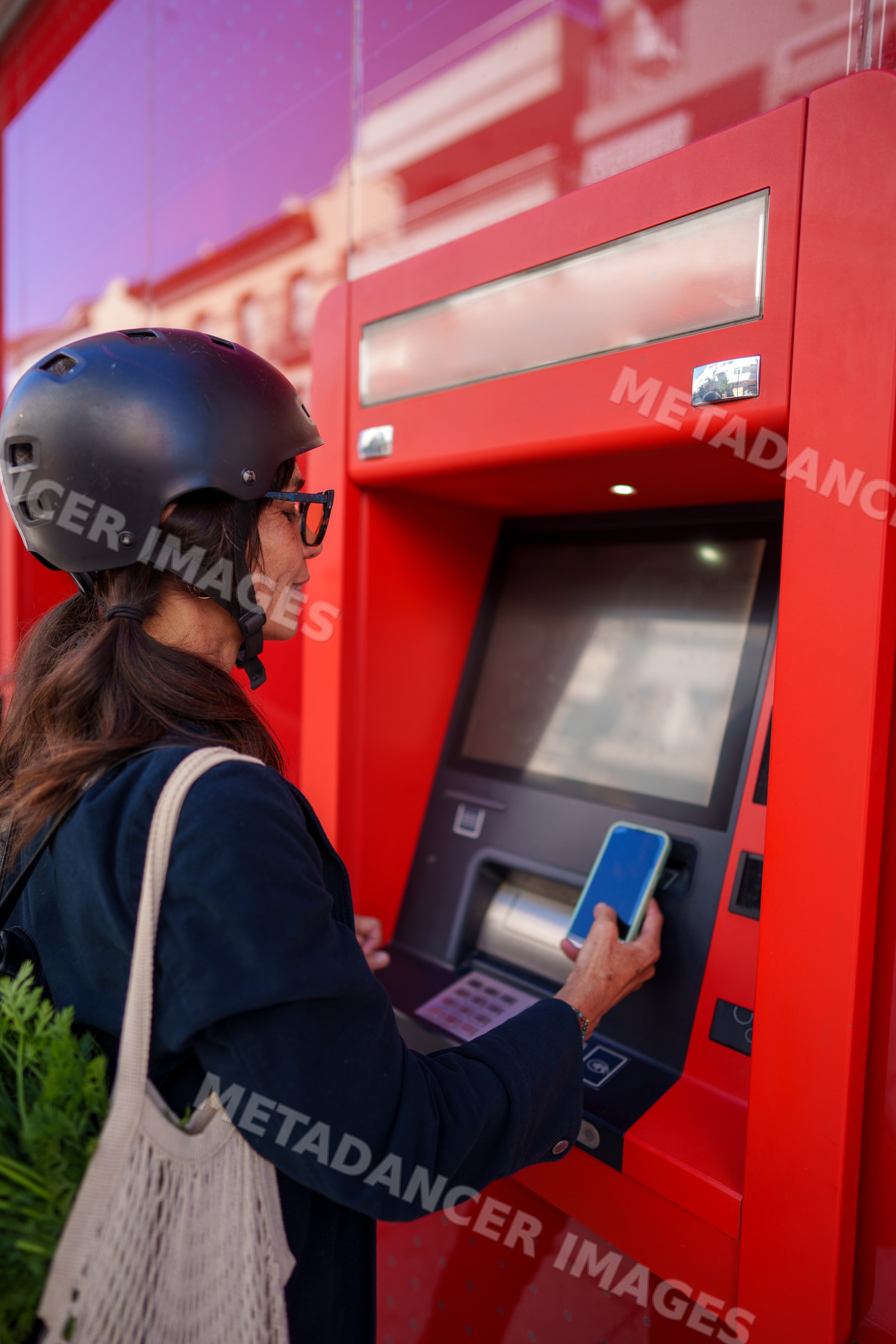 Hispanic woman using smartphone at red atm outdoors