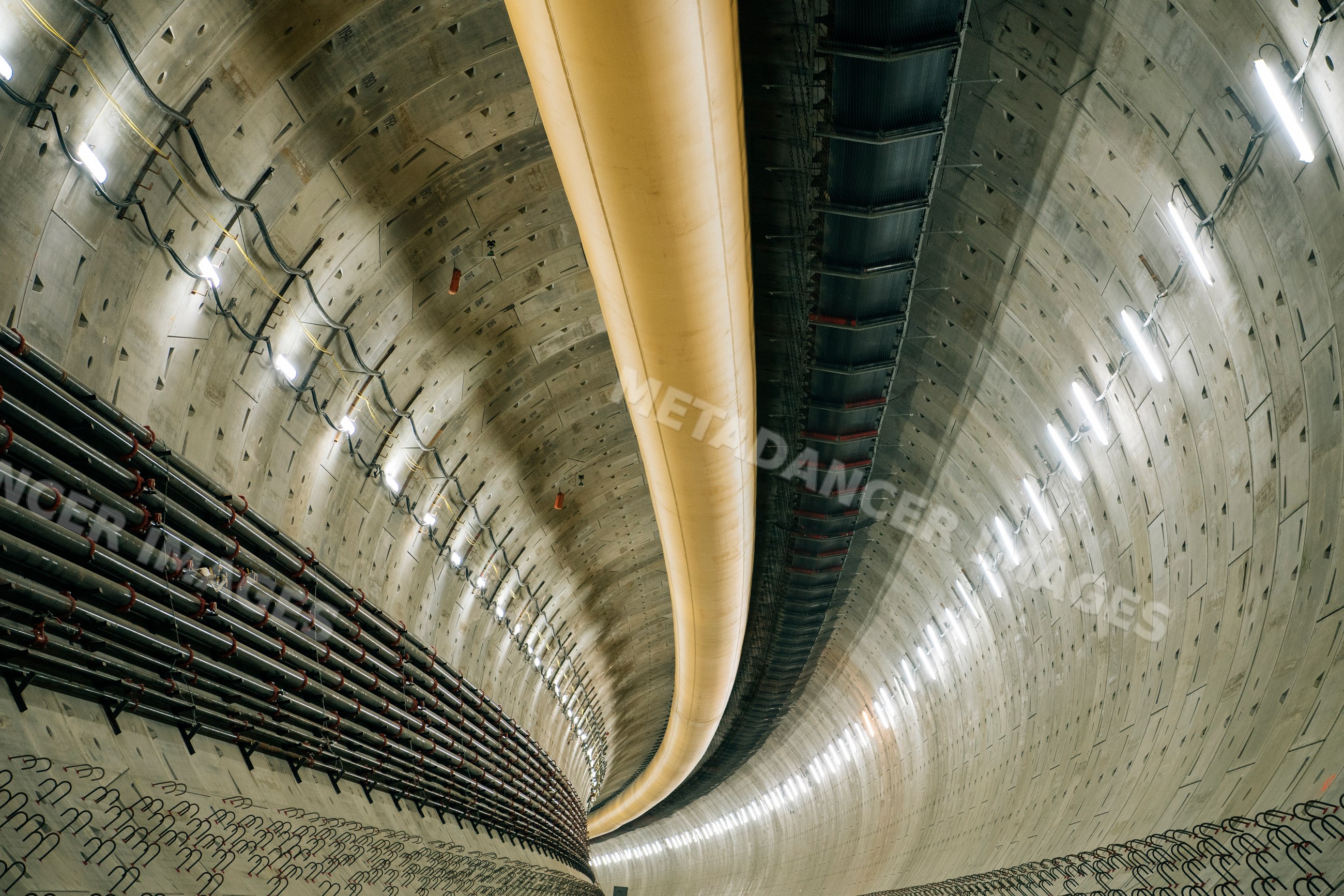 Interior of a large concrete tunnel with pipes and ventilation ducts