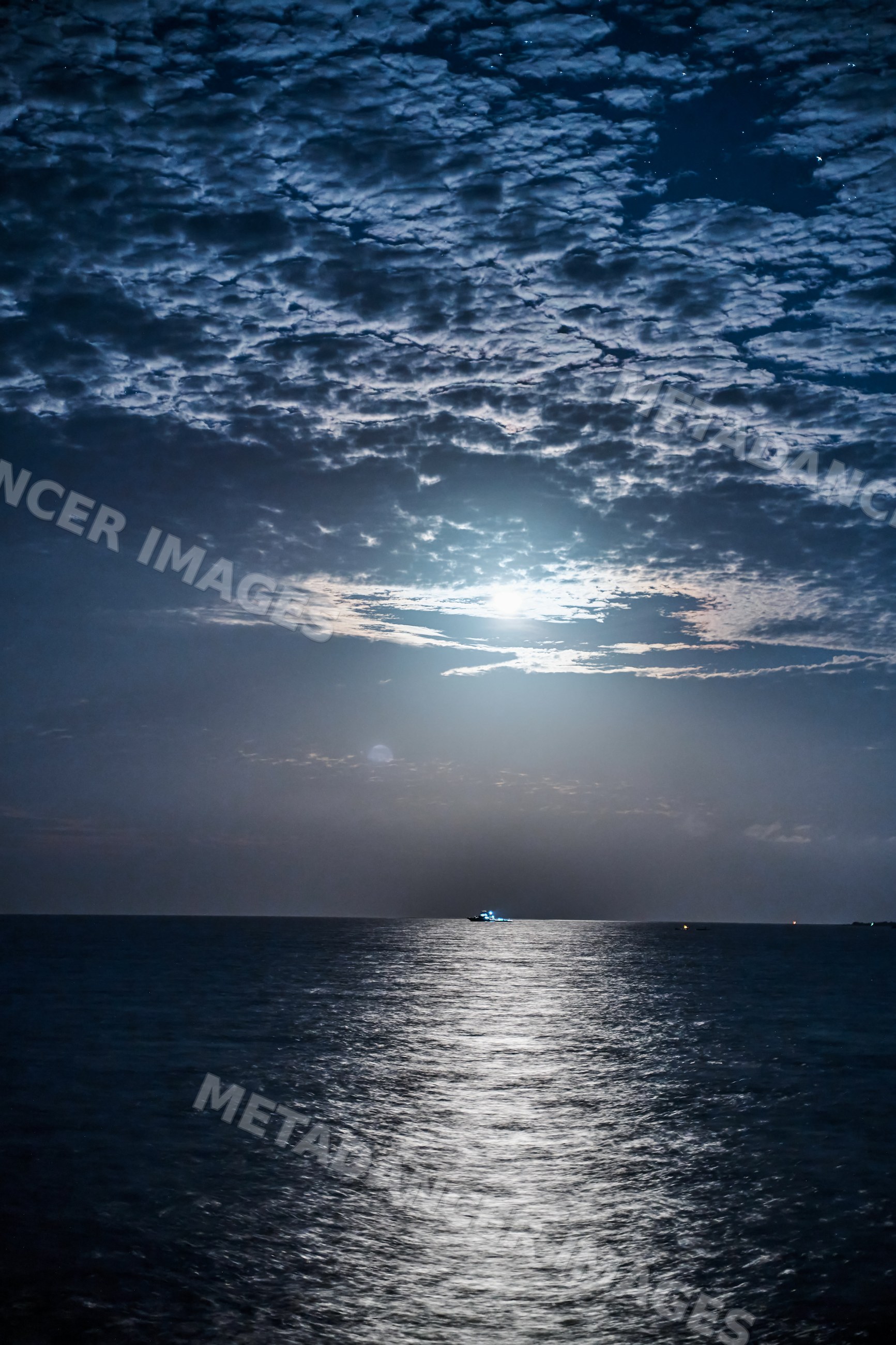 A boat illuminated by moonlight floats on the calm ocean