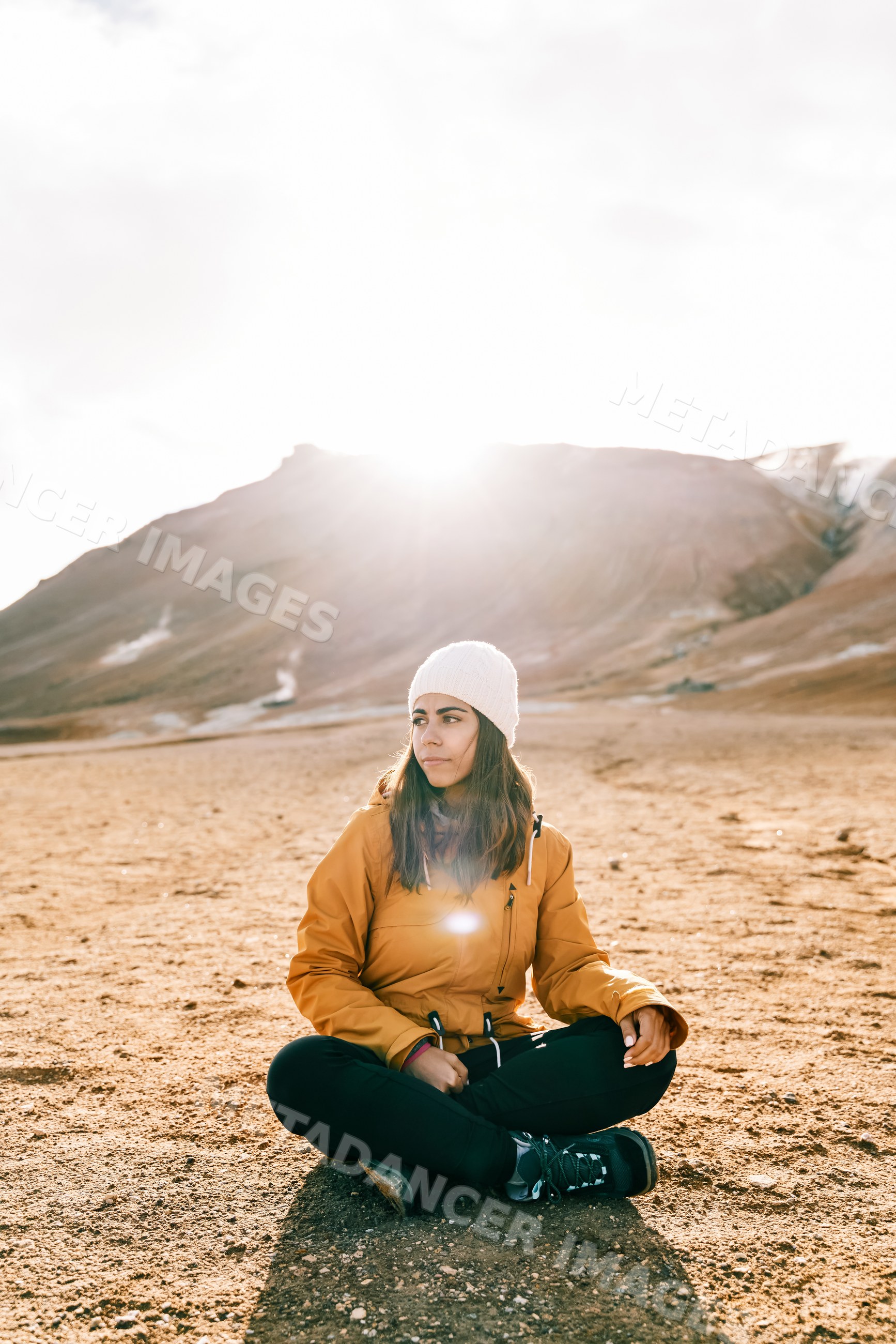 A white woman sits on rocky ground outdoors with mountains