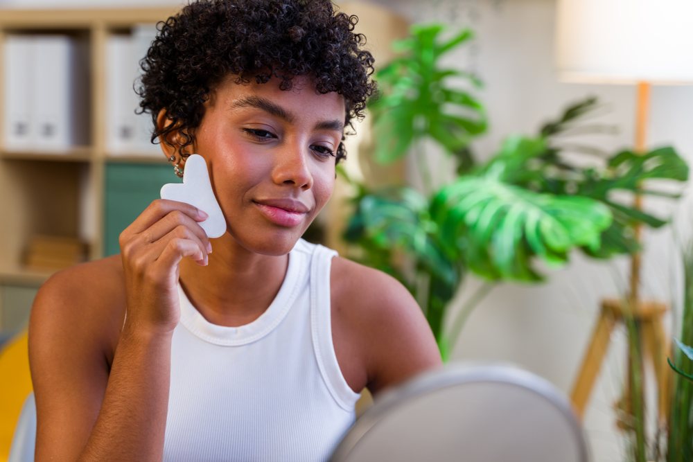 African American woman applying facial gua sha tool for skin care