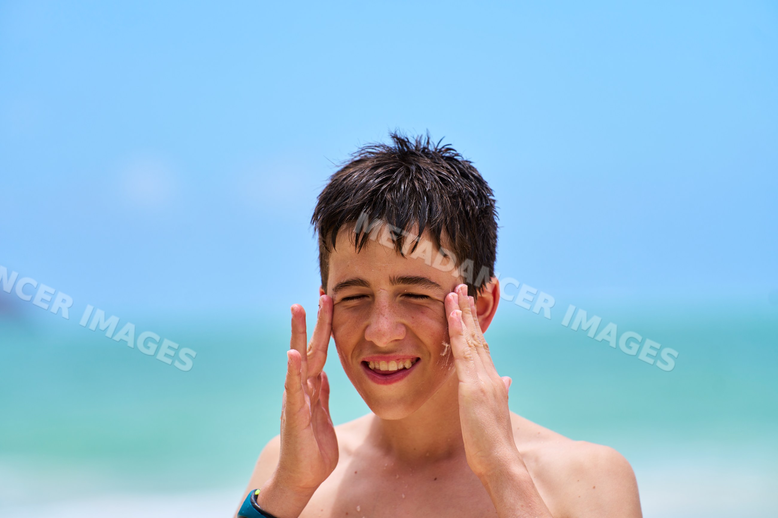 White boy applying sunscreen on beach by ocean on sunny day
