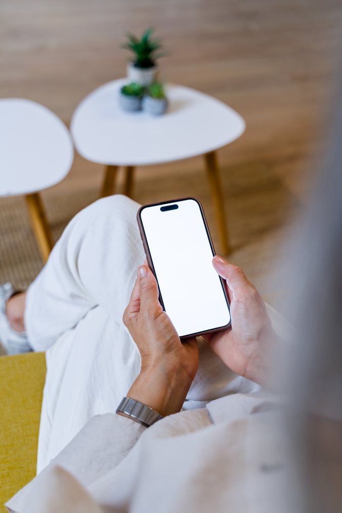 Person holding smartphone with white screen in modern indoor setting