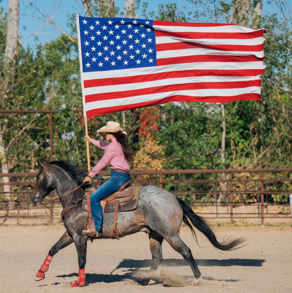 White woman riding horse holding american flag in Southwest USA arena
