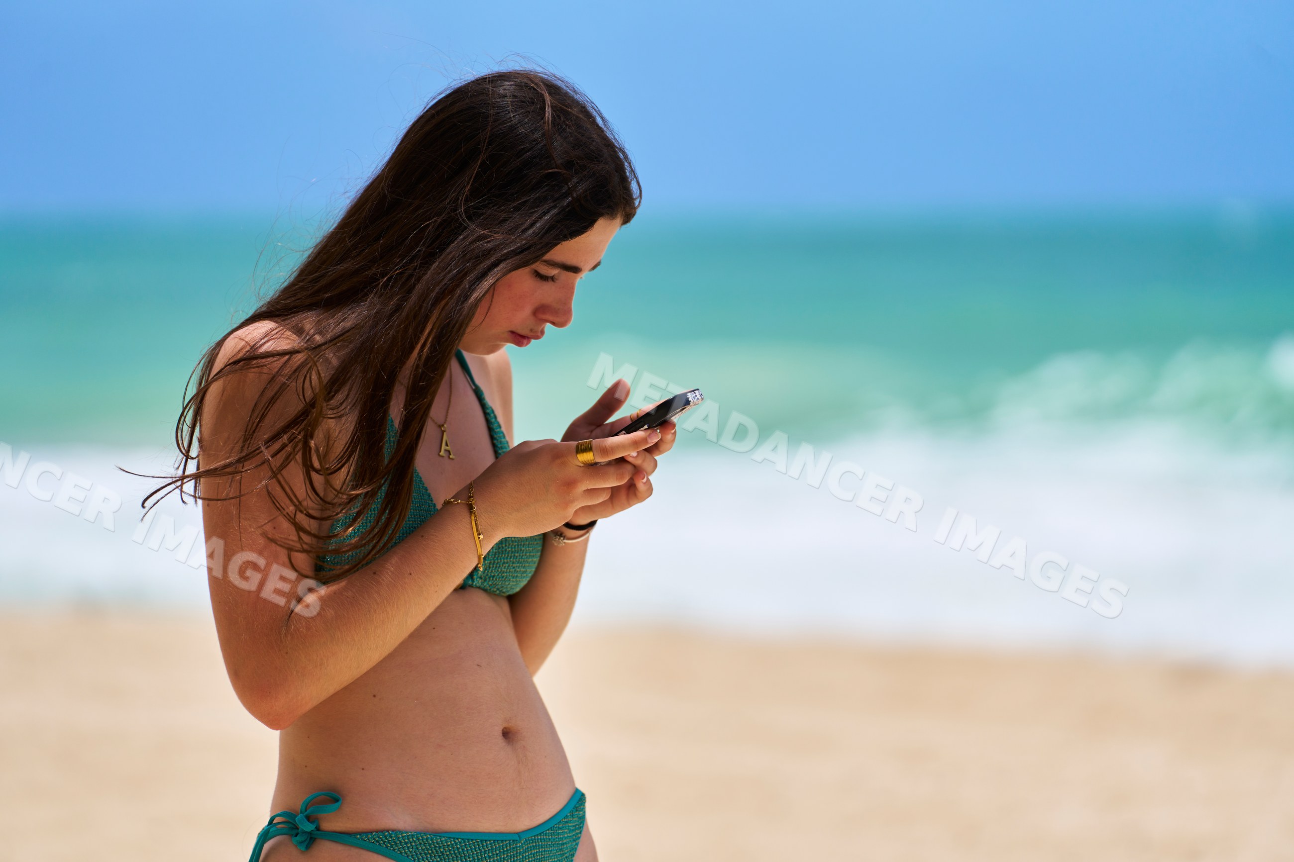 Teenage white girl in green swimsuit using smartphone on beach