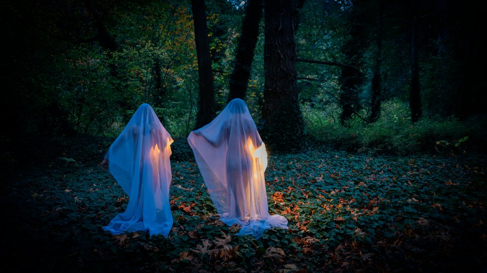 Two ghosts illuminated in blue light in dark forest at night