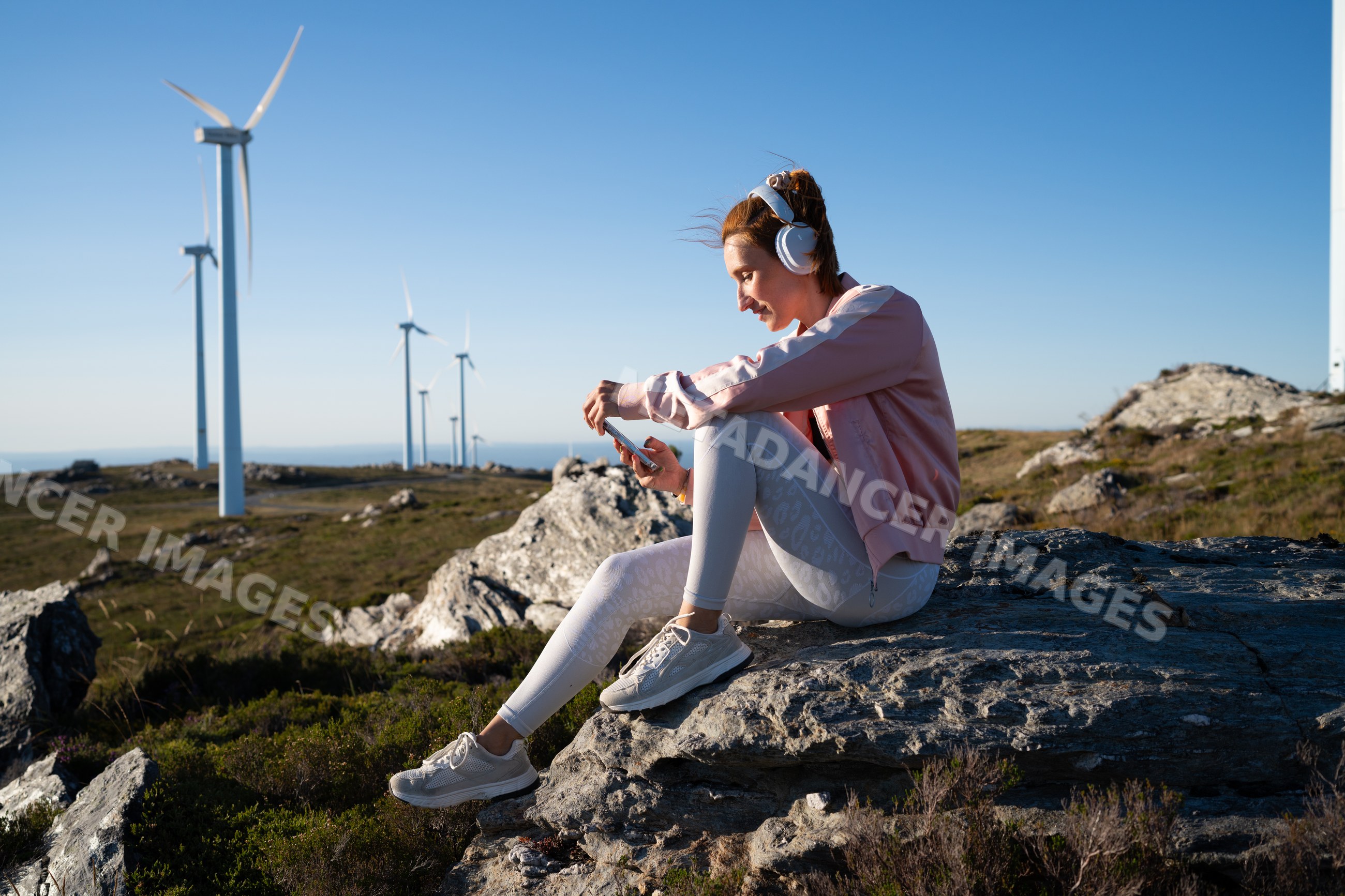 A white woman listens to music outdoors near wind turbines in Galicia
