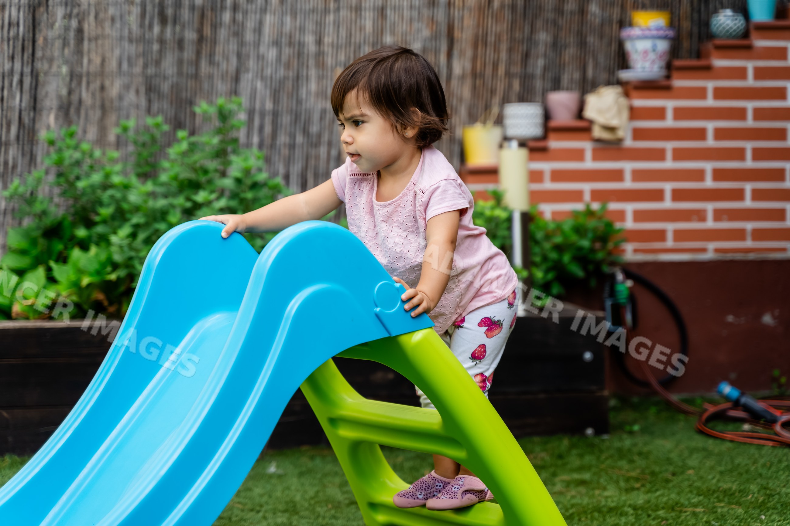 Toddler climbing plastic slide in backyard garden in Spain