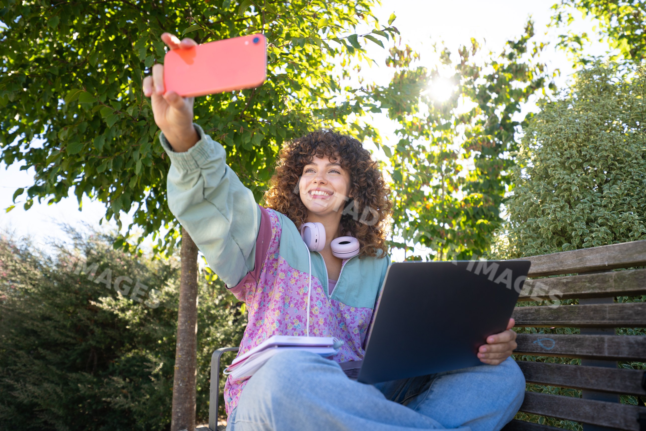 White woman taking selfie outdoors on bench with laptop and notebooks