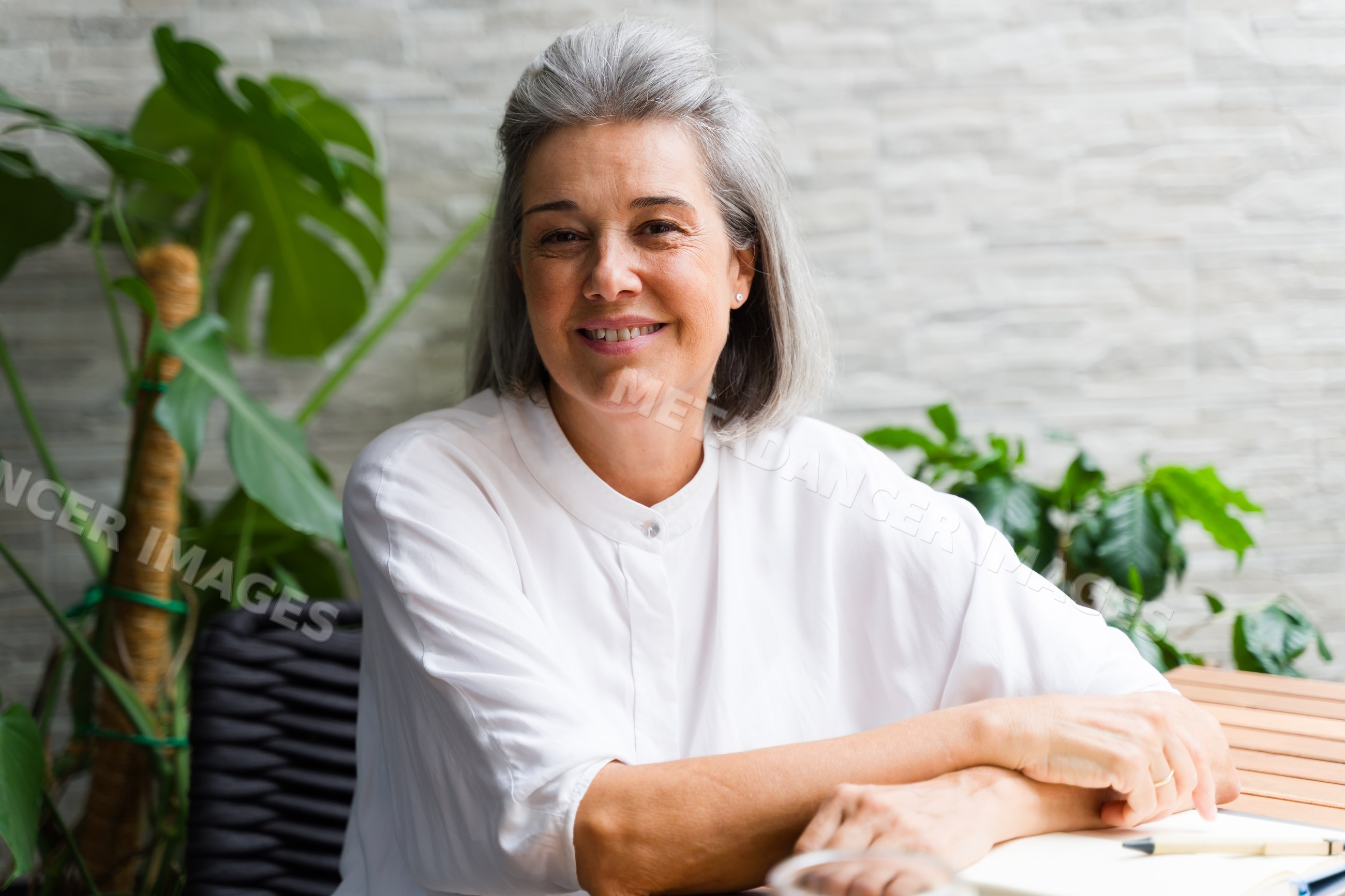 Mature white woman sitting indoors smiling with houseplants